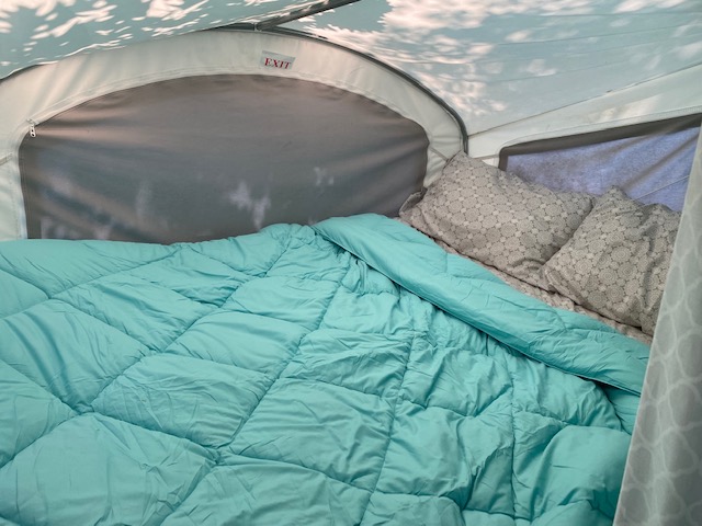Inside an RV rental: a cozy bed with a teal comforter and patterned pillows, under an "EXIT" sign. Perfect for camping adventures.. Skyline Bobcat 2012