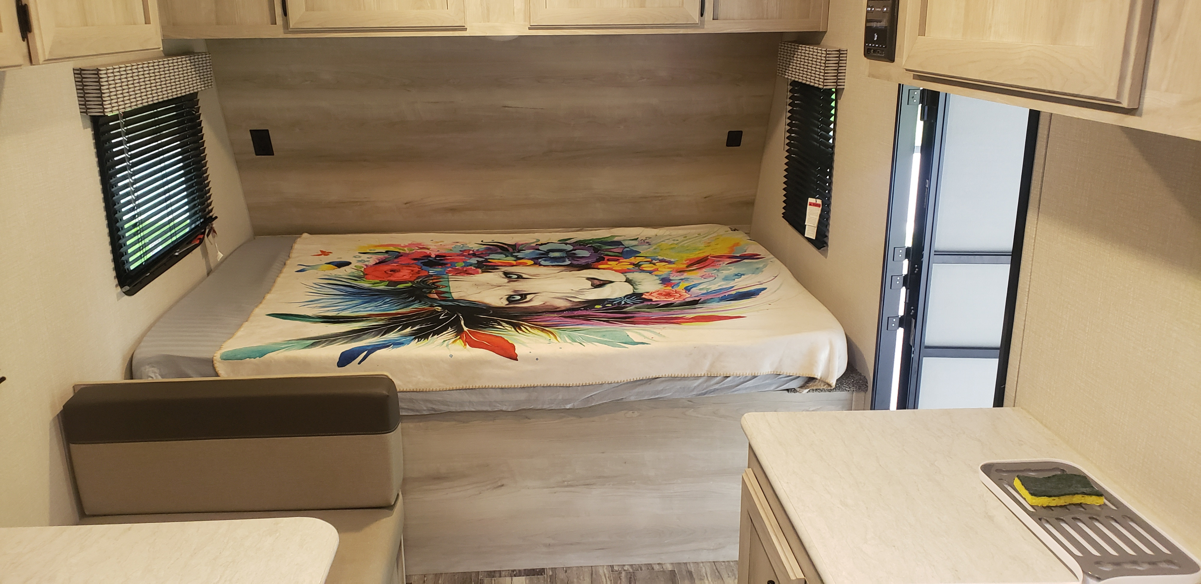 Explore this cozy RV rental interior: comfortable bed with unique blanket, dinette, and kitchen counter with sponge.. KZ Sportsmen 180BH 2021