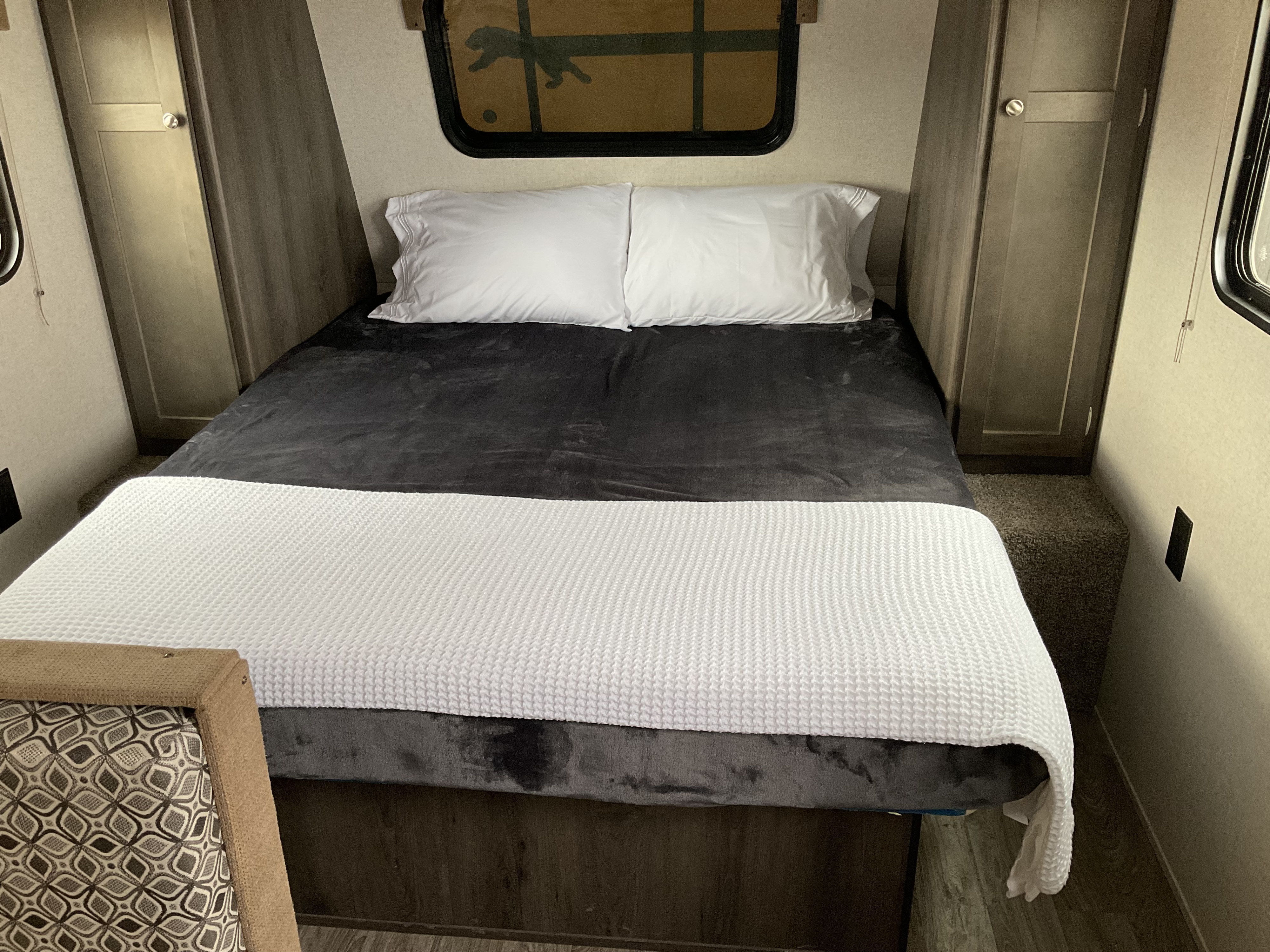Cozy RV rental bedroom with a neatly made bed, dark blanket, white pillows, and built-in storage on both sides.. Coachmen Clipper 2019