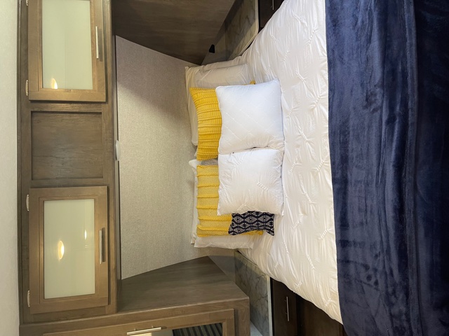 Cozy RV rental bedroom with white bedding, yellow pillows, a blue blanket, and built-in cabinets.. Dutchmen Coleman 2021