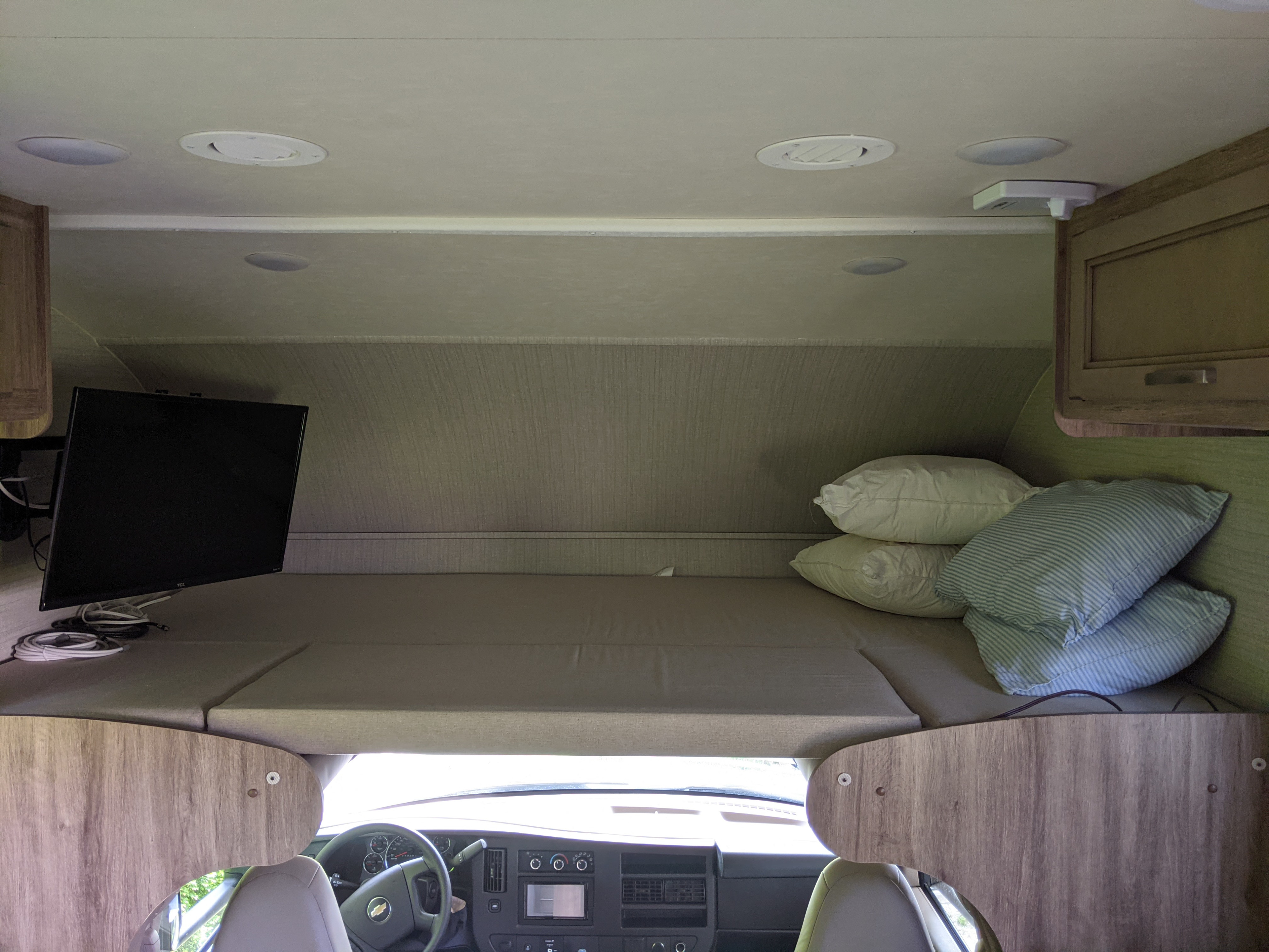 An RV rental's cab-over bunk, featuring a bed, TV, and view of the dashboard, ready for adventure.. Jayco Redhawk 2020