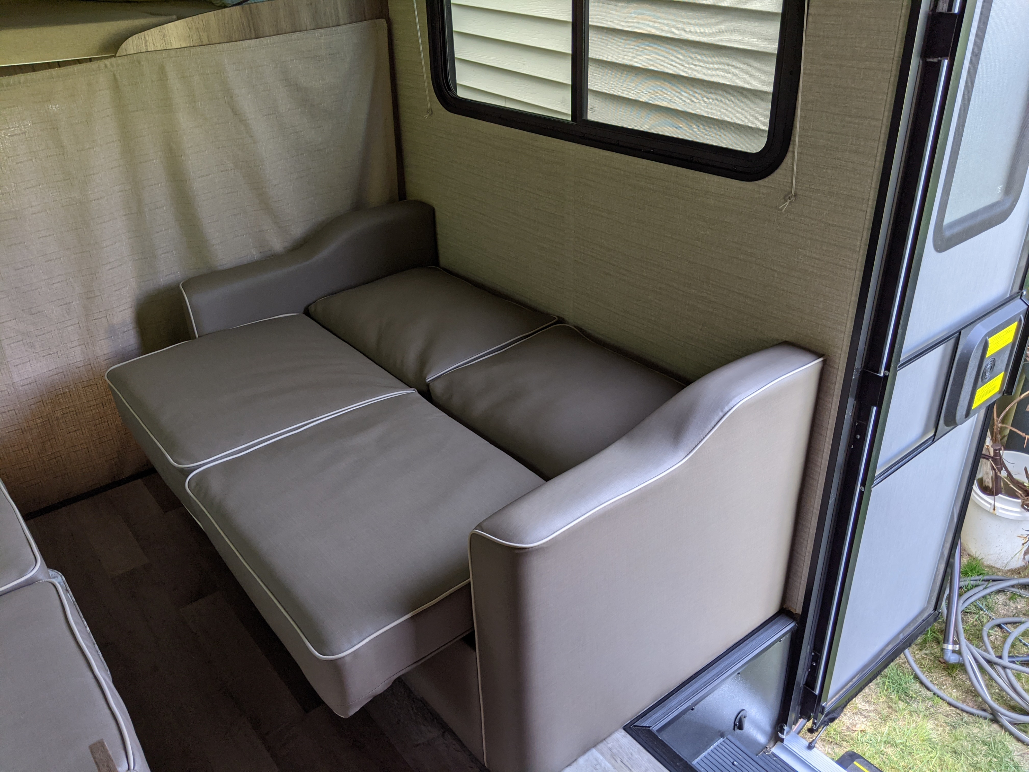 An RV rental's versatile interior with a gray sofa bed fully extended and an open side door.. Jayco Redhawk 2020