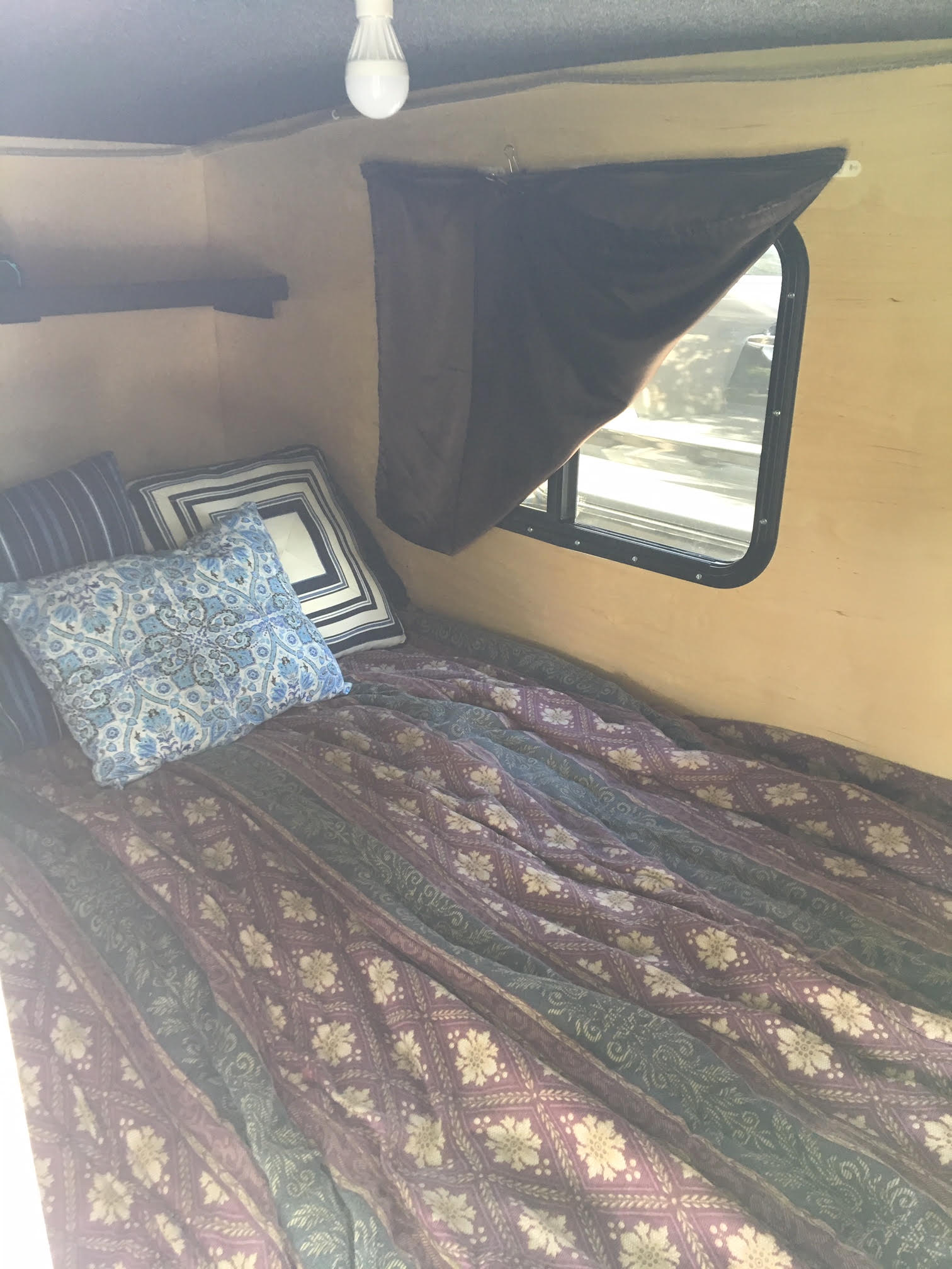 Cozy RV rental camper interior: bed with patterned bedding, pillows, window, shelf. Ideal for travel.. Runaway Campers Navigator 2017