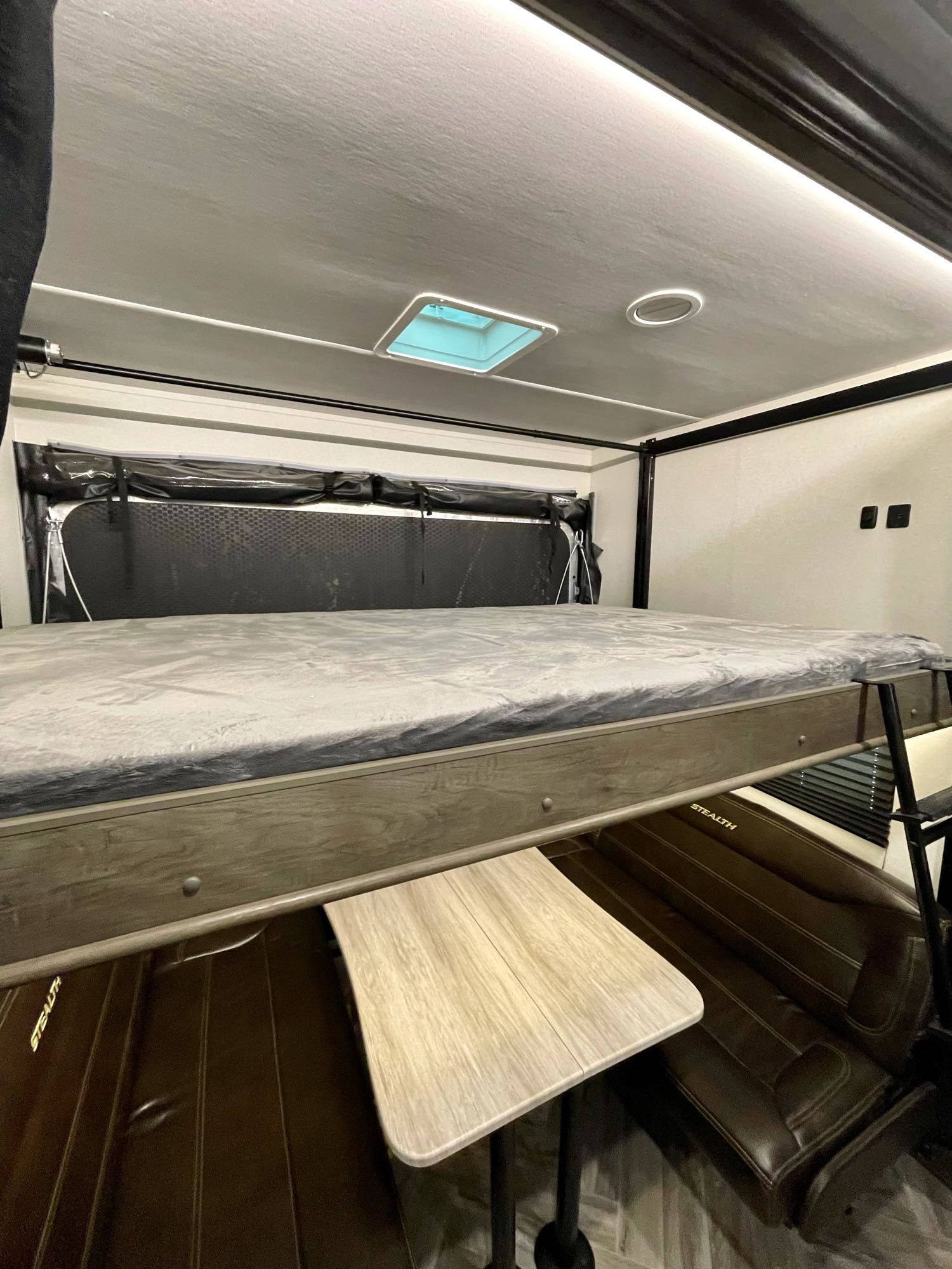 RV rental interior: Overhead bunk bed above dining table and bench seating. Perfect for family adventures in your Stealth RV.. Forest River Stealth 2021