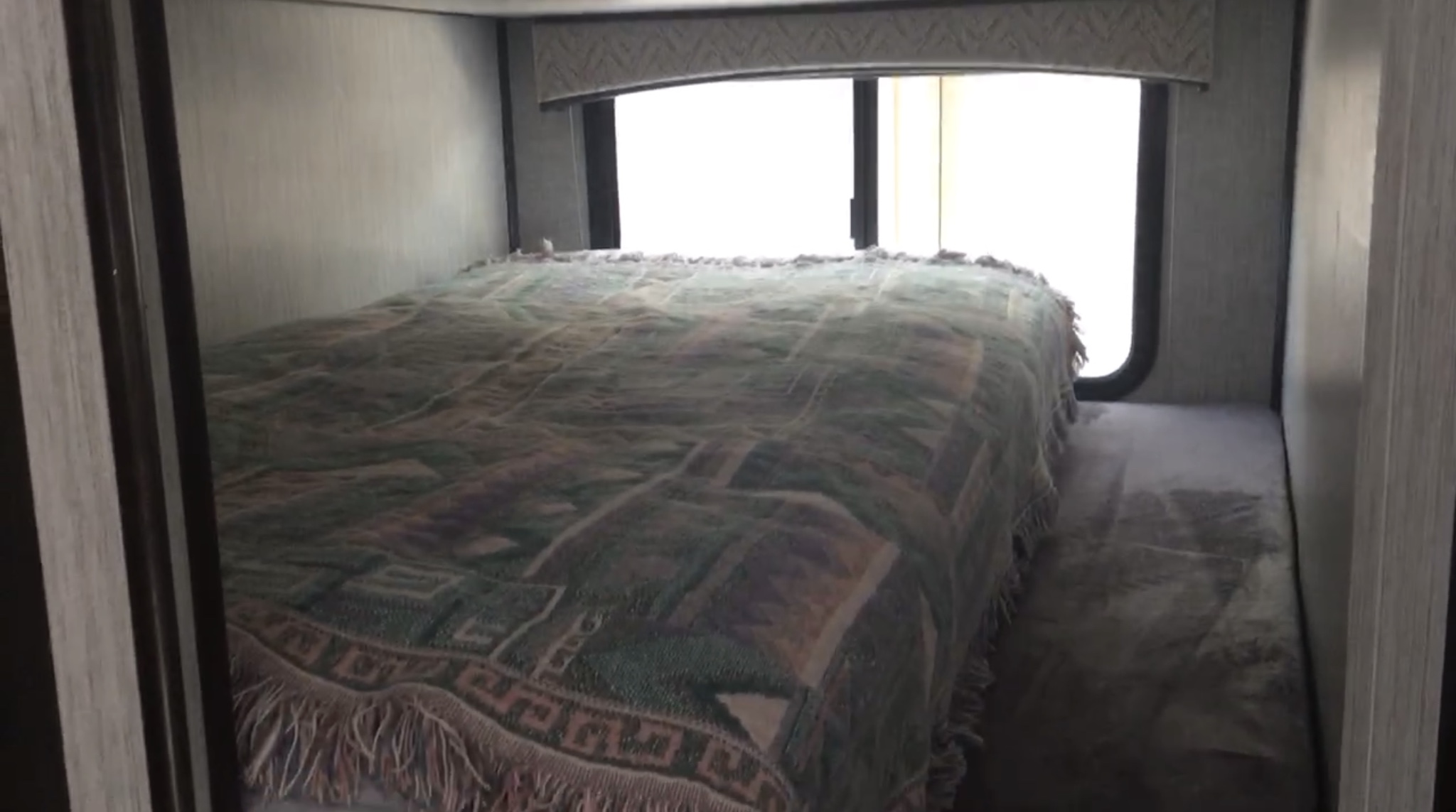 Inside an RV rental, this bedroom offers a bed with a patterned blanket, large window, and side bunk for comfort.. Heartland RVs Sundance Ultra Lite 2020