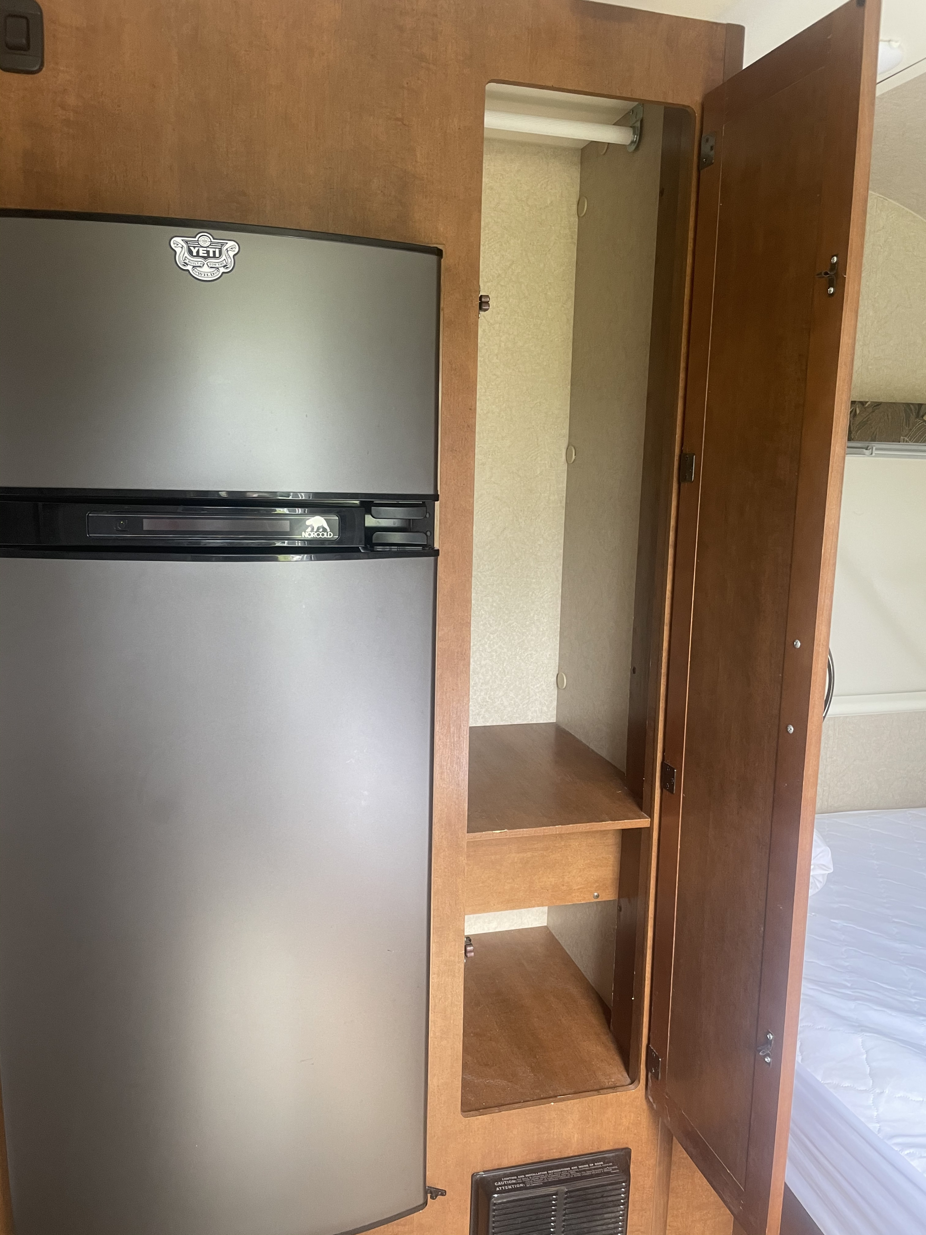 RV rental interior featuring a silver Norcold refrigerator with a Yeti sticker, and an open wood wardrobe with shelves and hanging space.. Lance 1575 2014