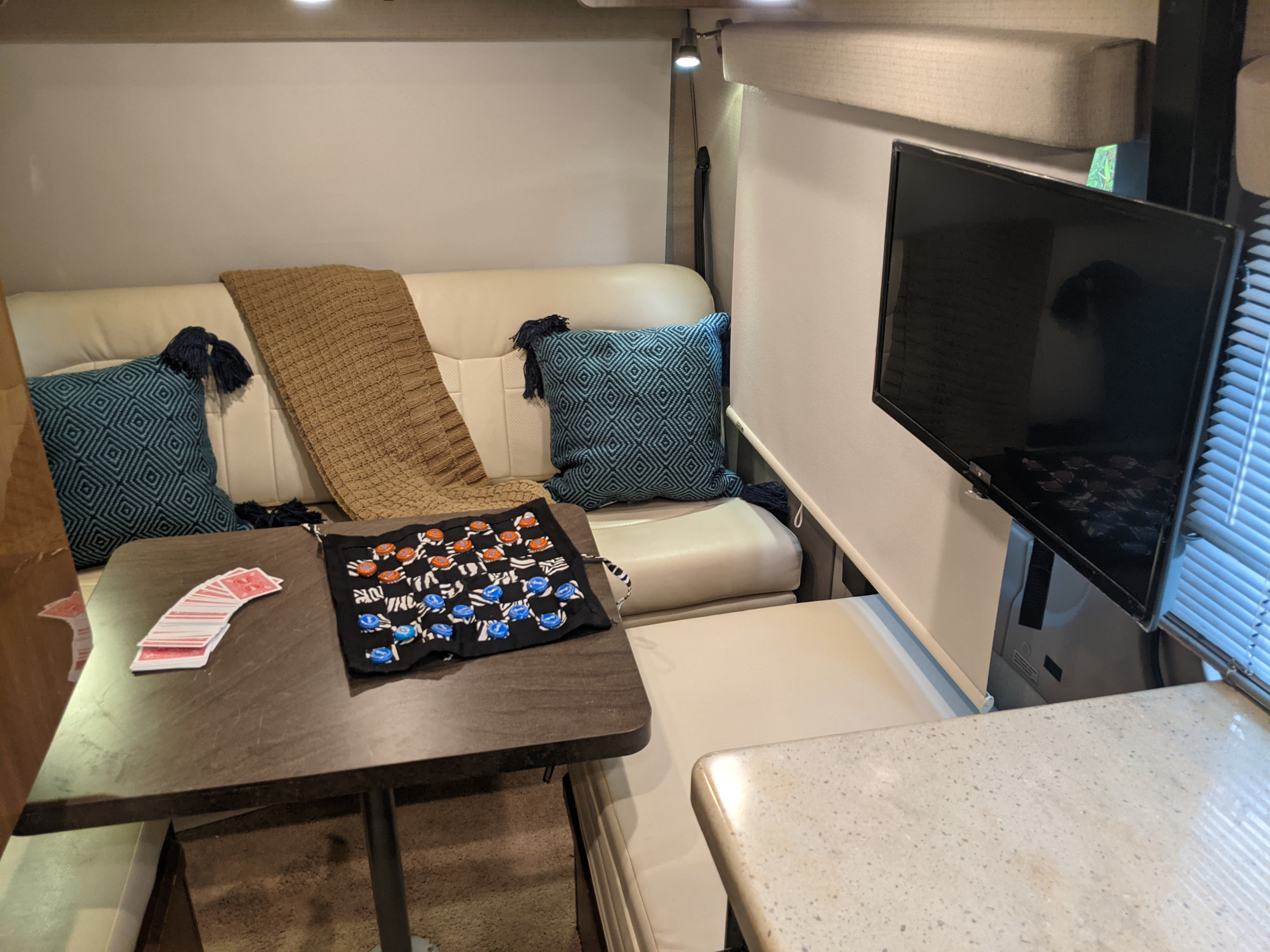 This RV rental interior features a cozy lounge, dining table with cards & a game, and a TV, providing a comfortable living space.. Winnebago Era 2015