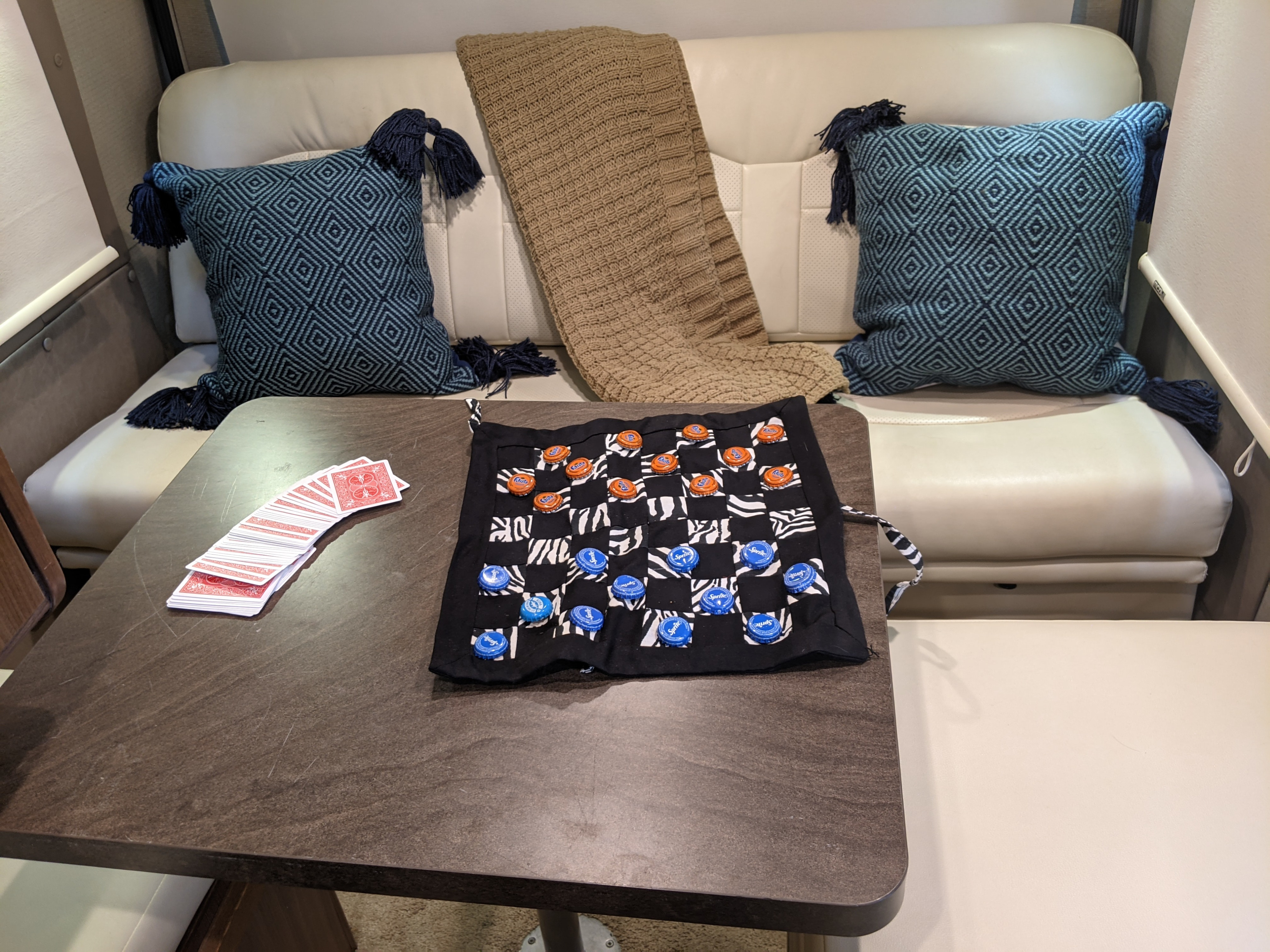 RV rental leisure: Playing cards & bottle cap checkers on a table, with a cozy couch, pillows, and blanket.. Winnebago Era 2015