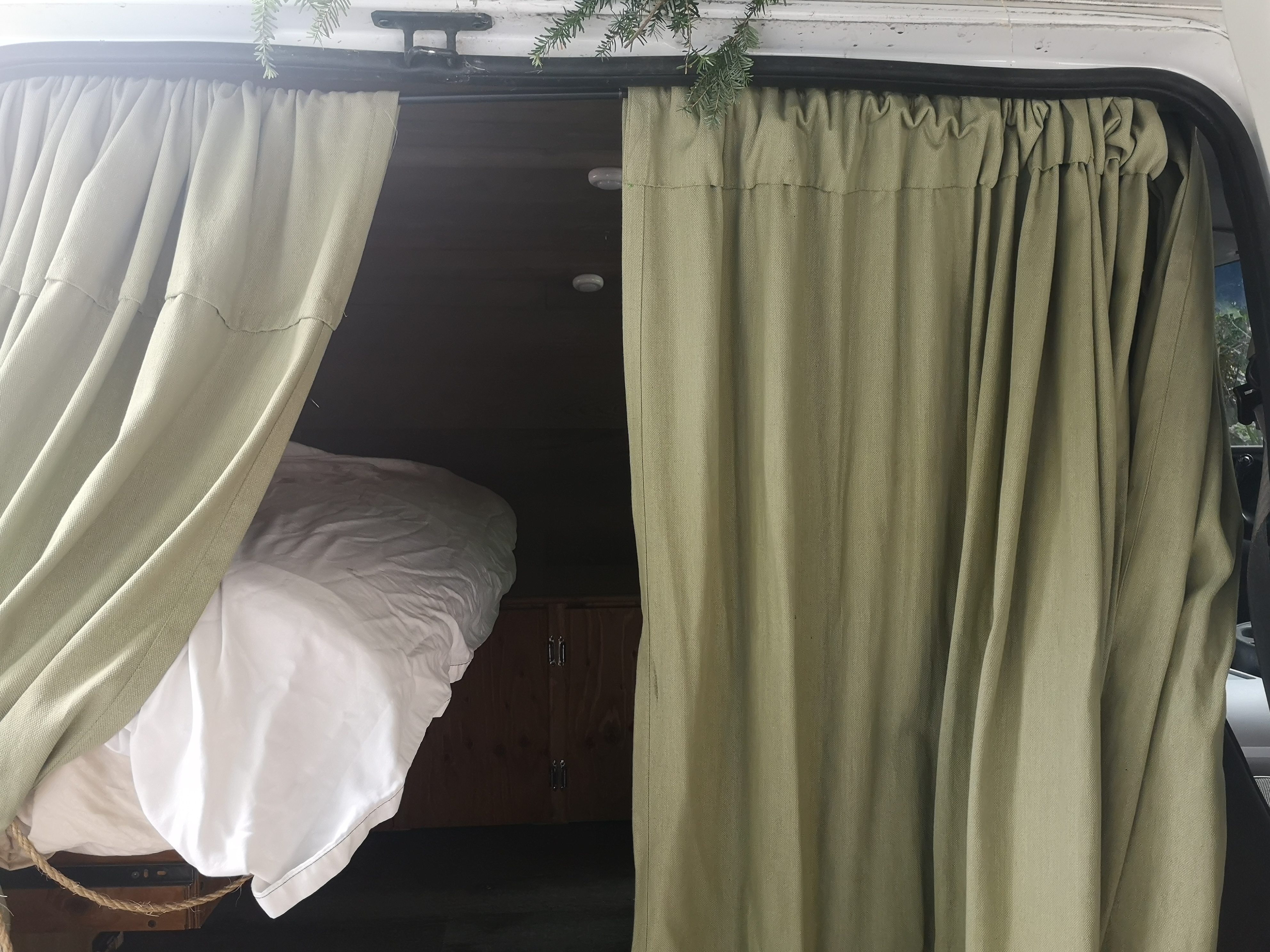 Cozy RV rental interior with curtains pulled back to show the bed. Perfect for van life adventures.. Ford Econolline 250s 1998