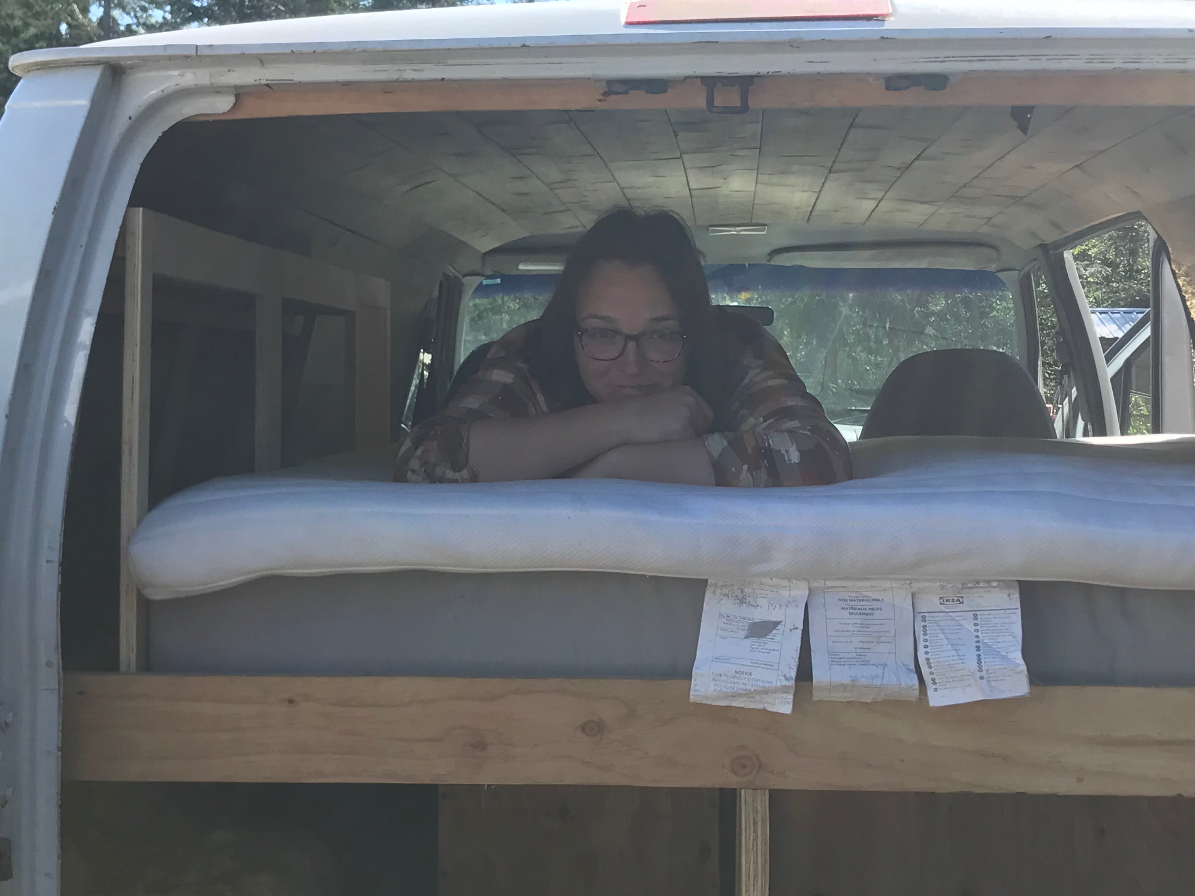 Cozy RV rental van conversion featuring a built-in bed. A person in glasses relaxes on the mattress inside.. Ford Econolline 250s 1998