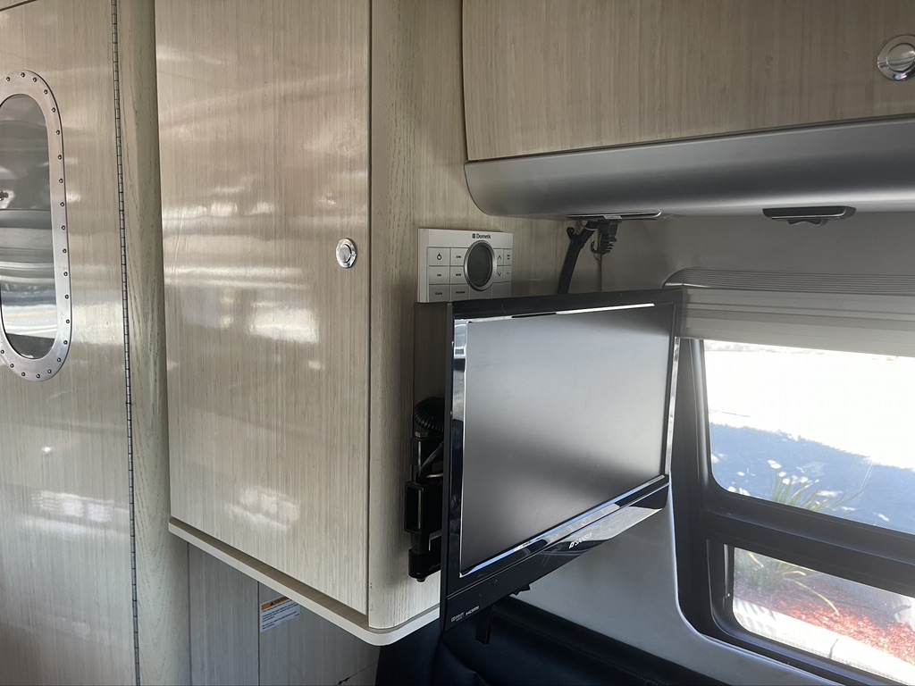 RV rental interior: light wood cabinets, wall-mounted TV, Dometic control panel, and unique oval window. A comfortable space.. Airstream Interstate 2013