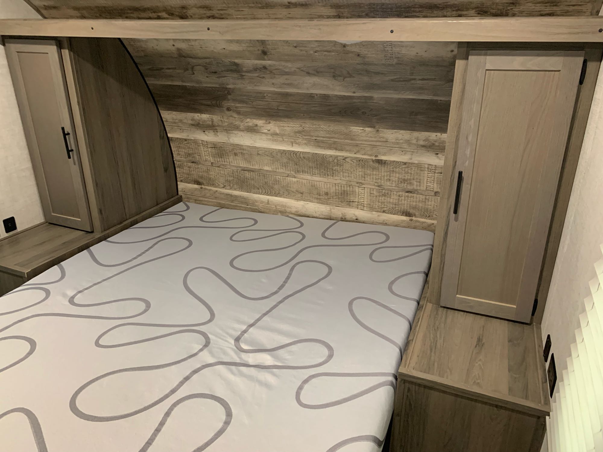 Inside an RV rental: a compact bedroom with a bed, side cabinets, and a rustic wood headboard.. Gulf Stream Kingsport 2021