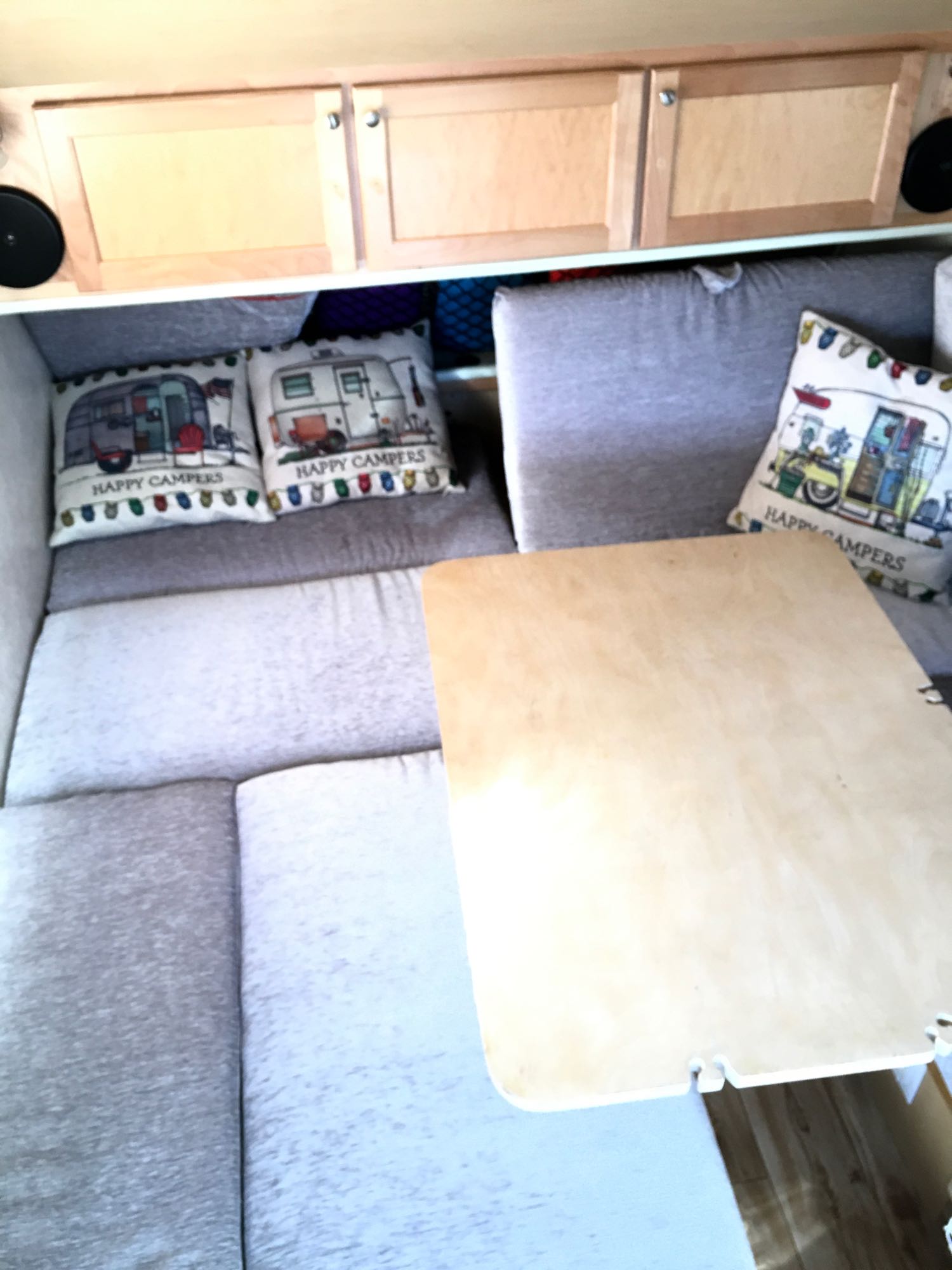 View inside an RV rental showing comfy grey seating, 'Happy Campers' pillows, a wooden table, and storage cabinets.. T@B 320S 2016