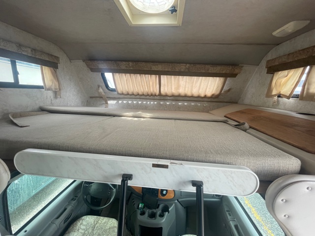 Spacious RV rental interior: a comfortable cab-over bunk, windows, and curtains, offering a cozy sleeping area for your travels.. Fleetwood Tioga 2000
