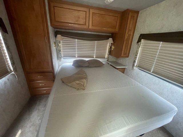 RV rental interior: bedroom with queen bed, wood storage cabinets, windows, and textured walls.. Fleetwood Tioga 2000