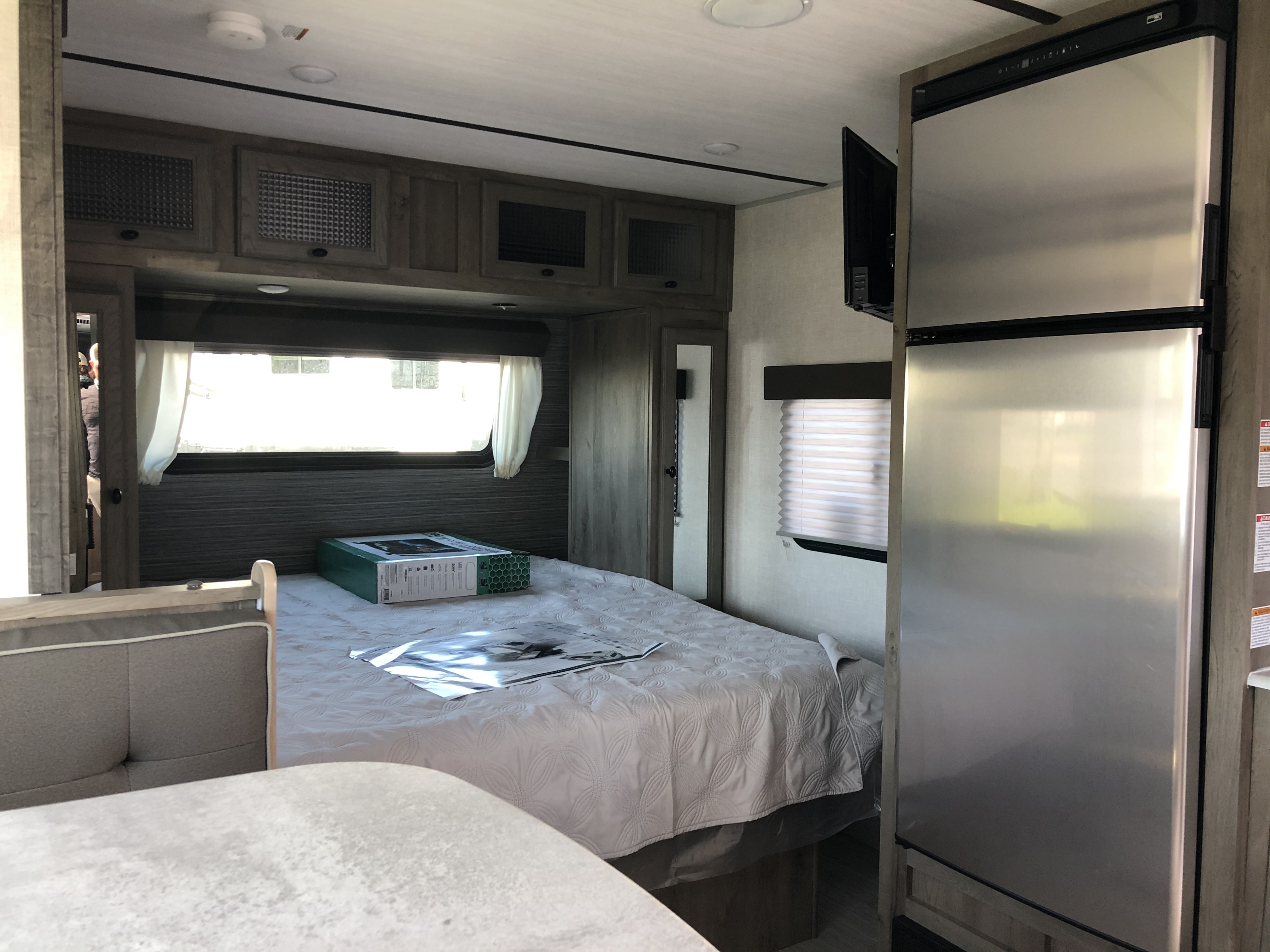 RV rental interior view: a bedroom with overhead cabinets, large bed, and compact kitchen with fridge and TV.. Forest River Surveyor 2021