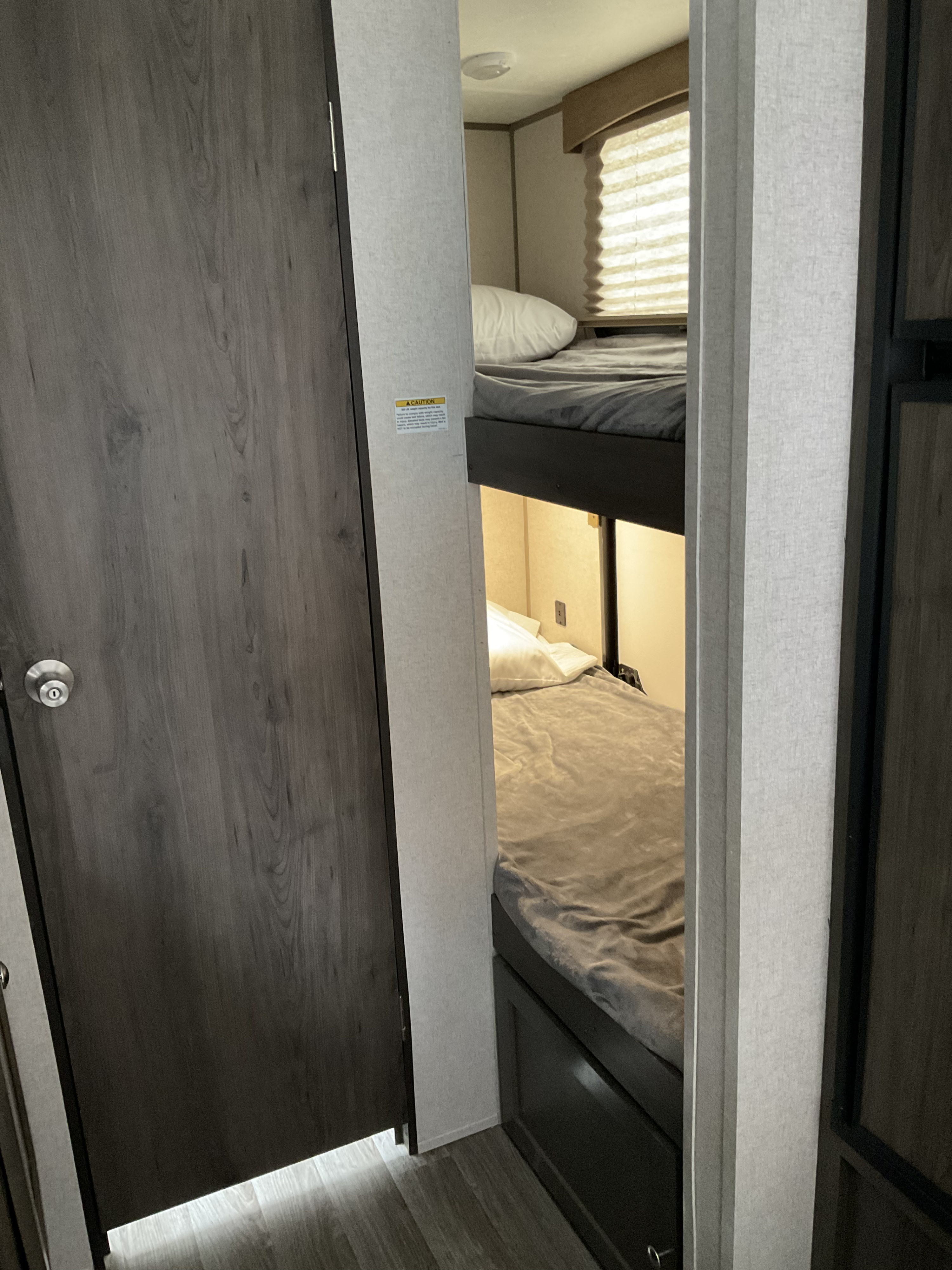 Inside an RV rental: view of two bunk beds, made up with pillows and blankets, and a dark wooden door on the left.. Coachmen Clipper 2019