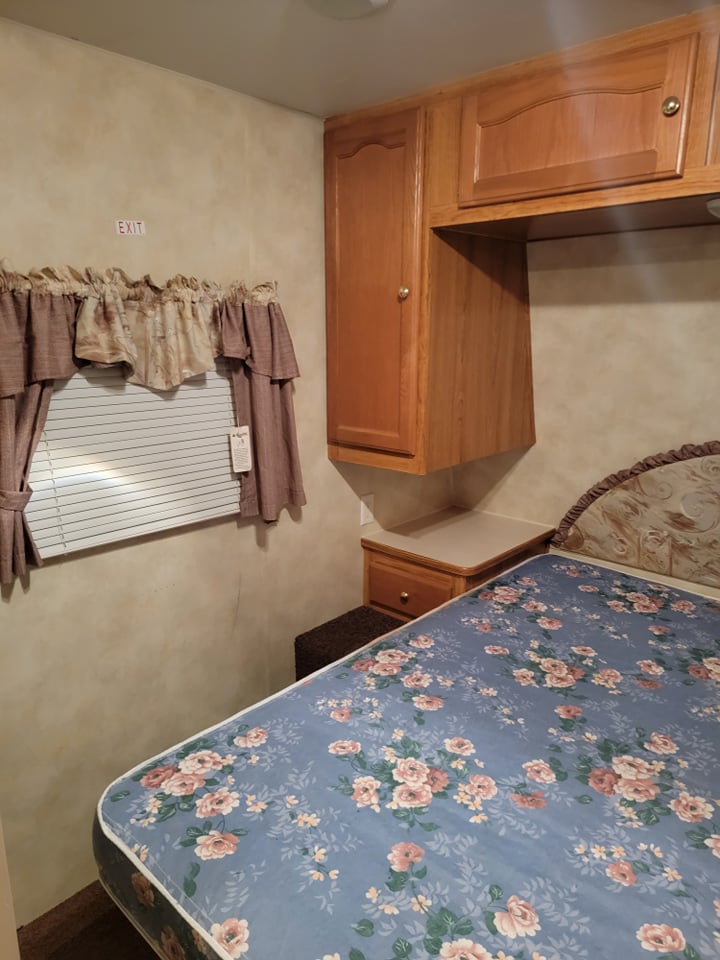 This RV rental bedroom offers a floral bed, window with curtains, and wooden cabinets for a comfortable stay.. Palomino Puma 2005