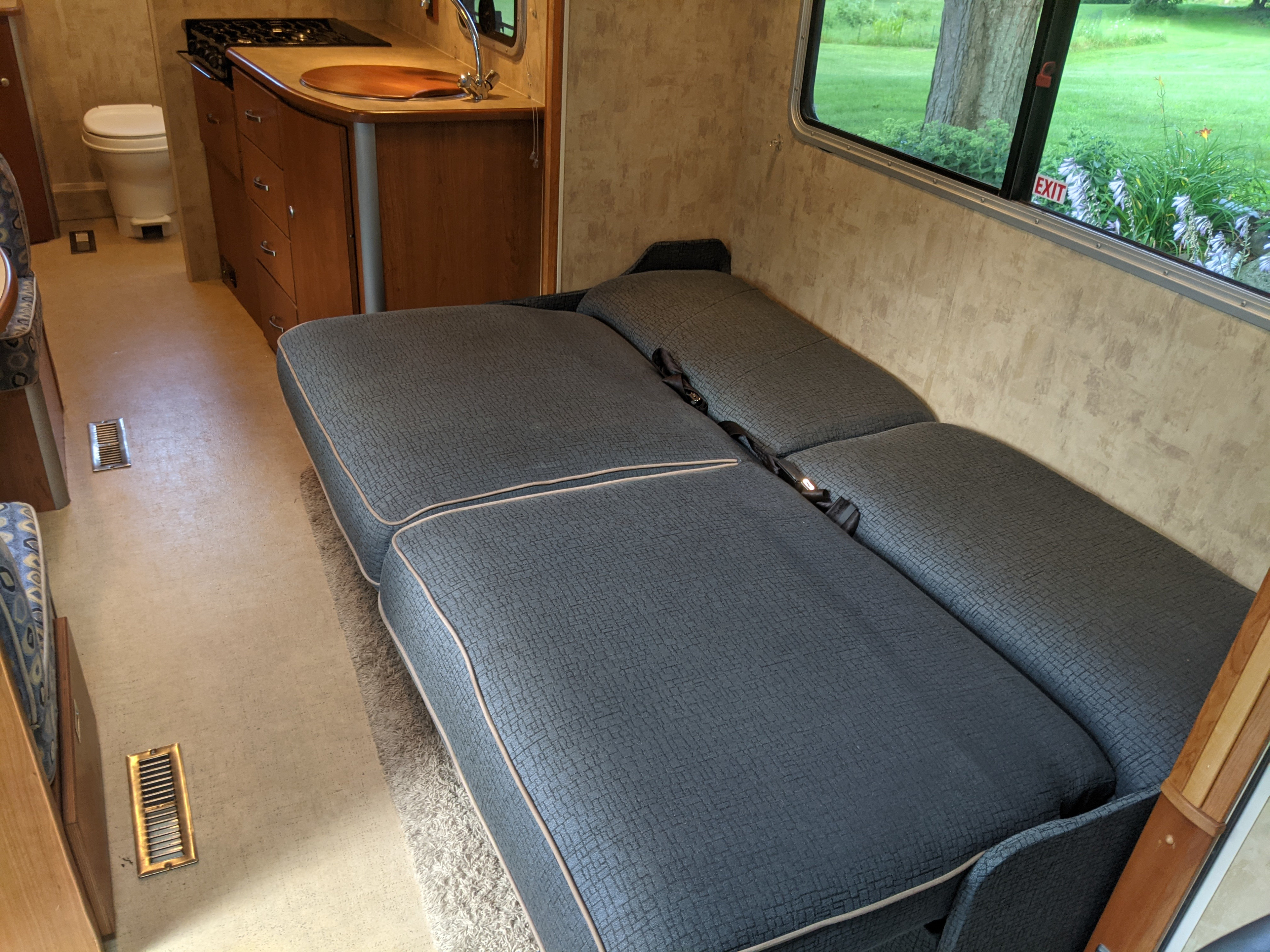 Compact RV rental living space featuring a convertible sofa bed, kitchenette with sink/stove, and a small toilet. Ideal for road trips.. Winnebago View 2007
