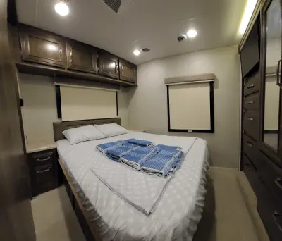 Clean RV rental bedroom with queen bed, overhead cabinets, and fresh towels. Perfect for your next adventure.. Entegra Coach Esteem 2021