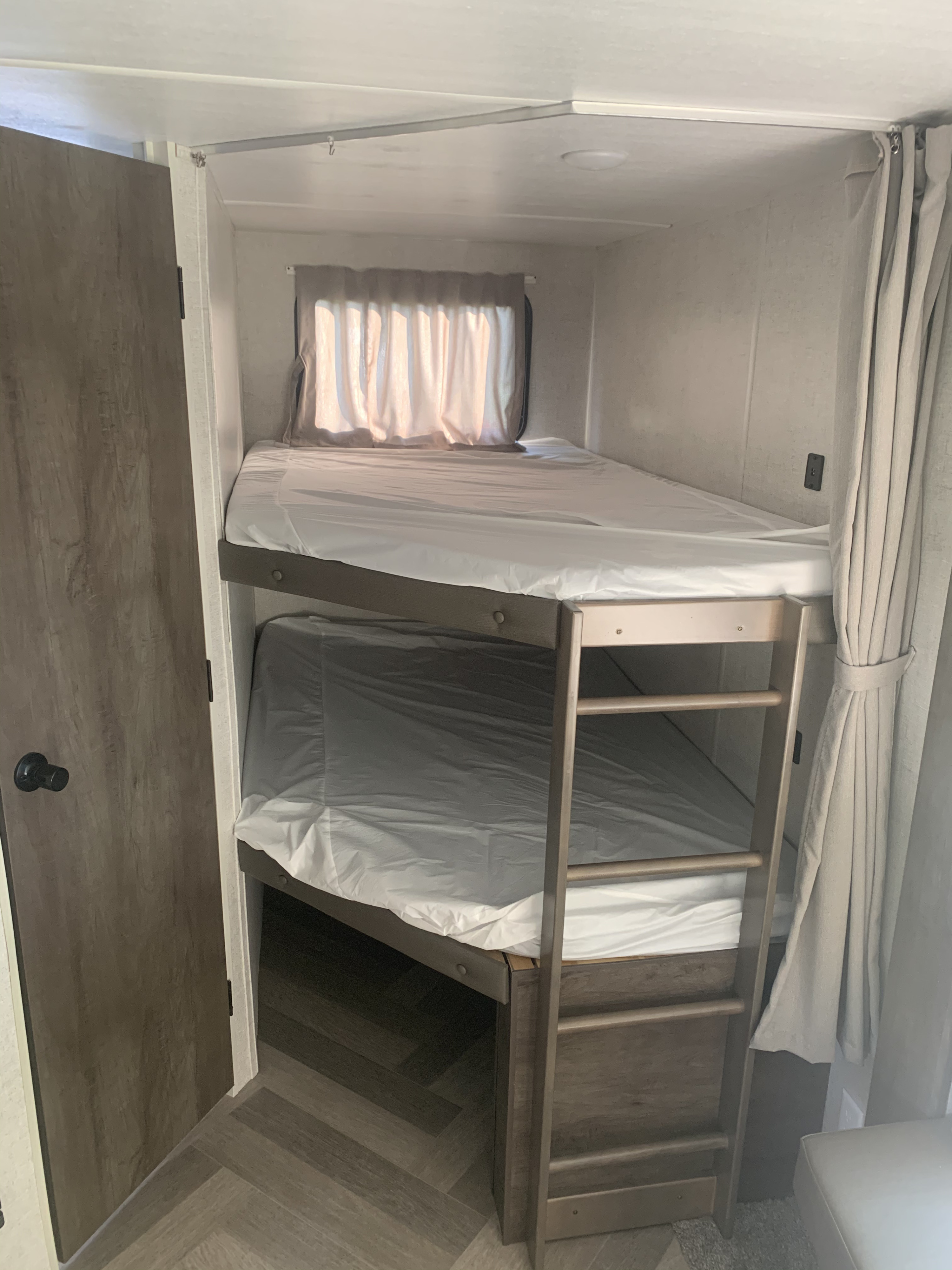 RV rental's bunk beds: a compact, clean sleeping area with a ladder, window, and fresh white linens.. Forest River Wildwood 2020