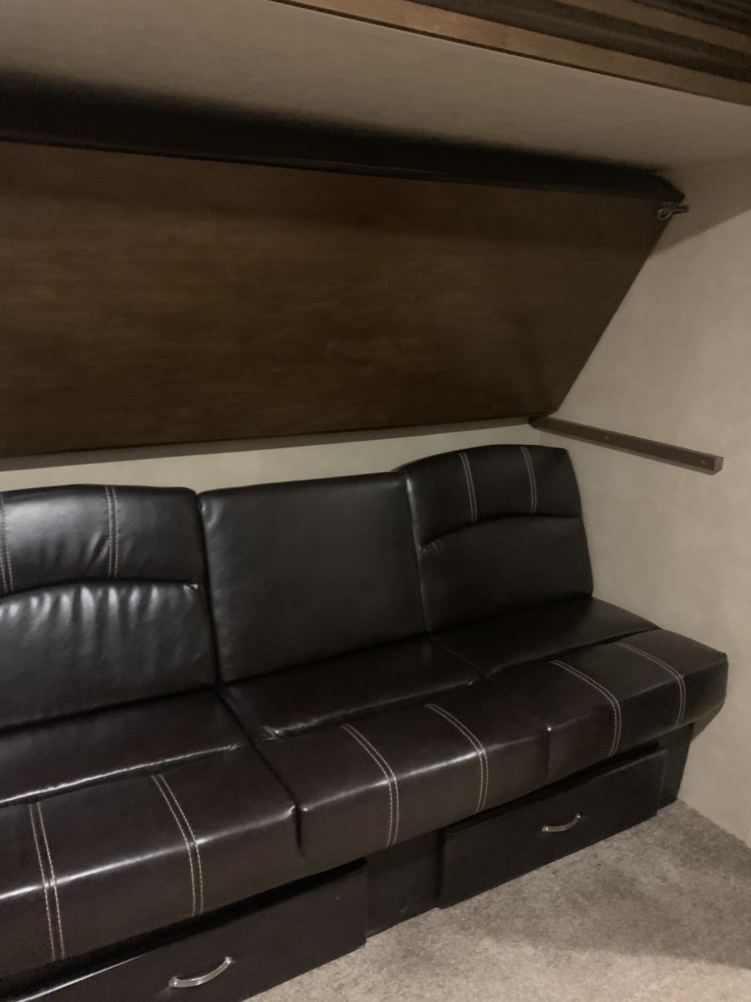 Interior of an RV rental: a dark brown leatherette sofa with white stitching, under-seat storage, and an upper bunk.. Forest River heritage glen q312bud 2017