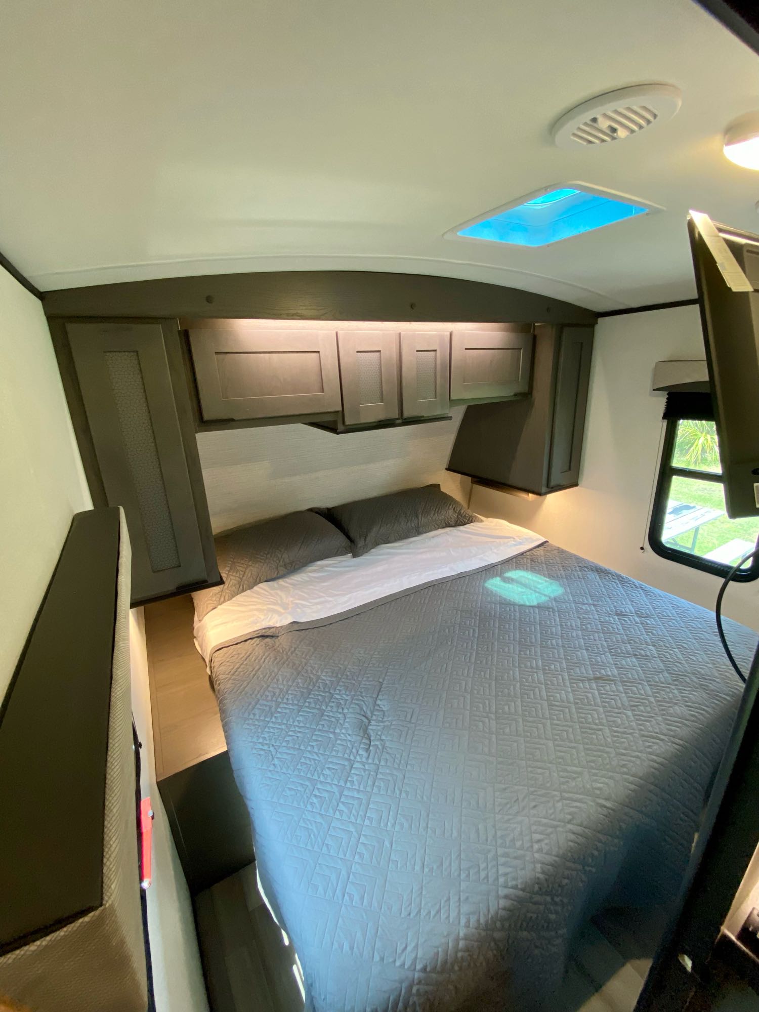 Bright RV rental bedroom featuring a queen bed, dark overhead cabinets, a ceiling skylight, and a window with outdoor view.. Cruiser Rv Corp EL310 2021