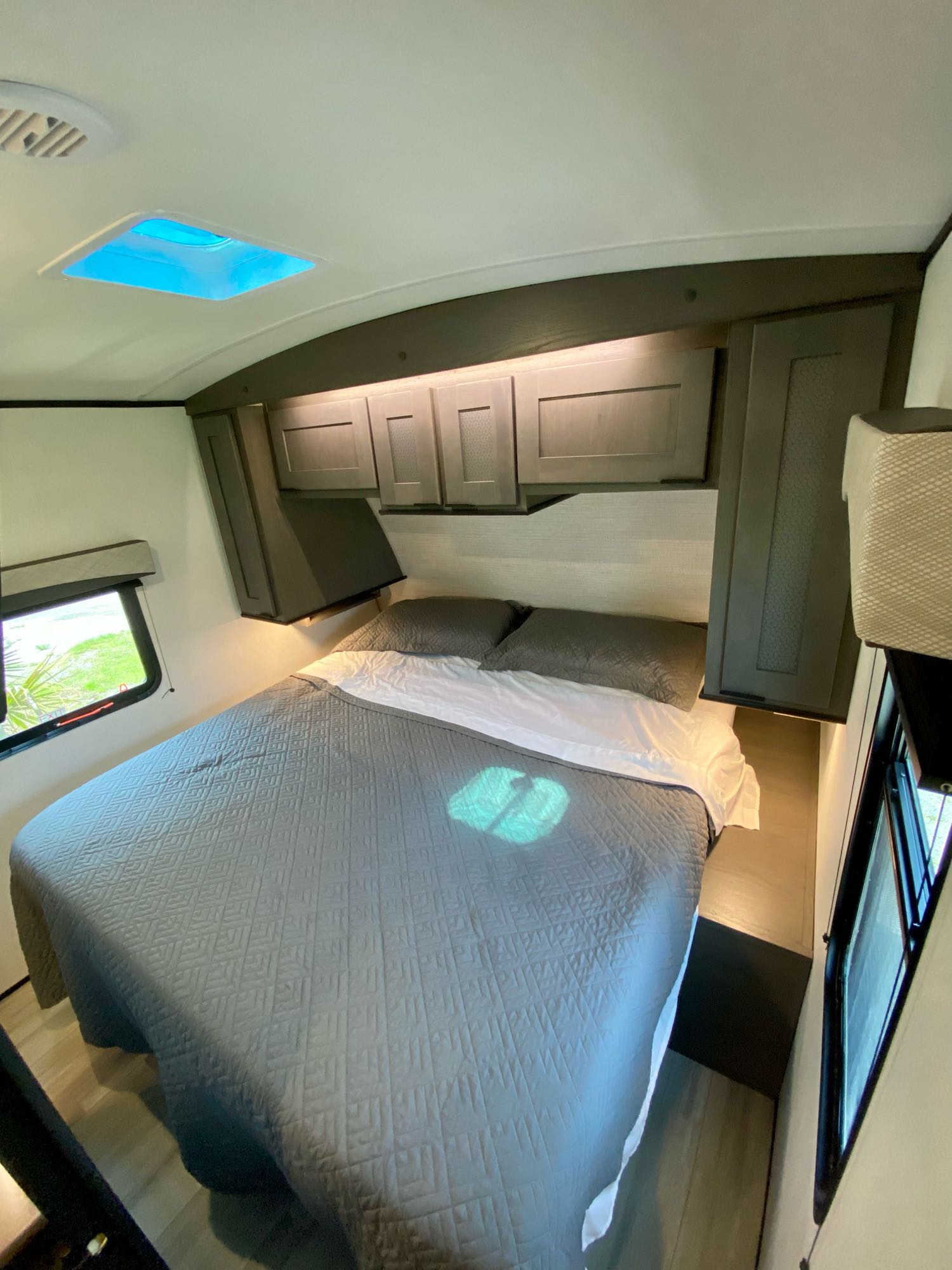 RV rental bedroom: a compact space with a cozy bed, dark overhead cabinets, and bright skylight above.. Cruiser Rv Corp EL310 2021