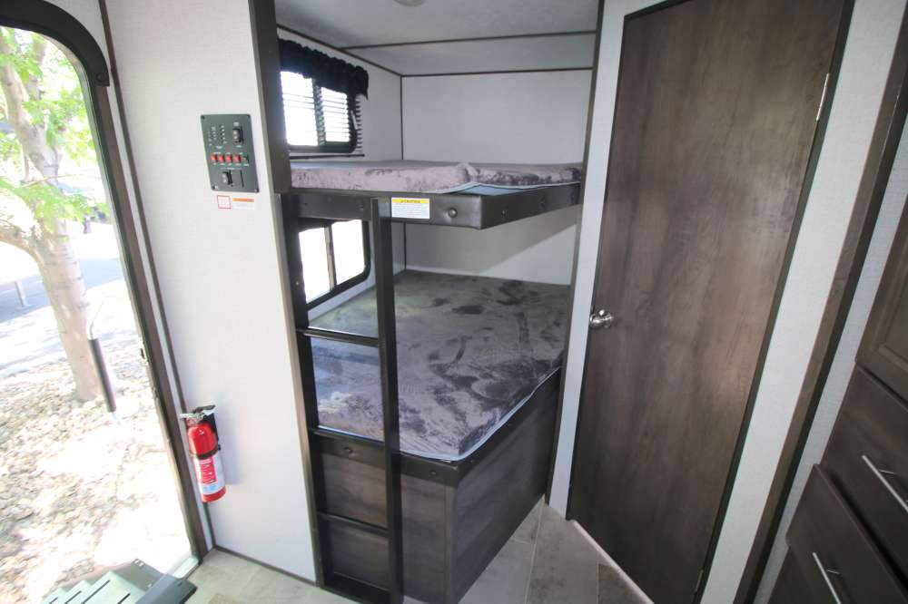 RV rental interior: Two compact bunk beds with mattresses, a window, and a safety fire extinguisher near the entry.. Coleman Other 2021
