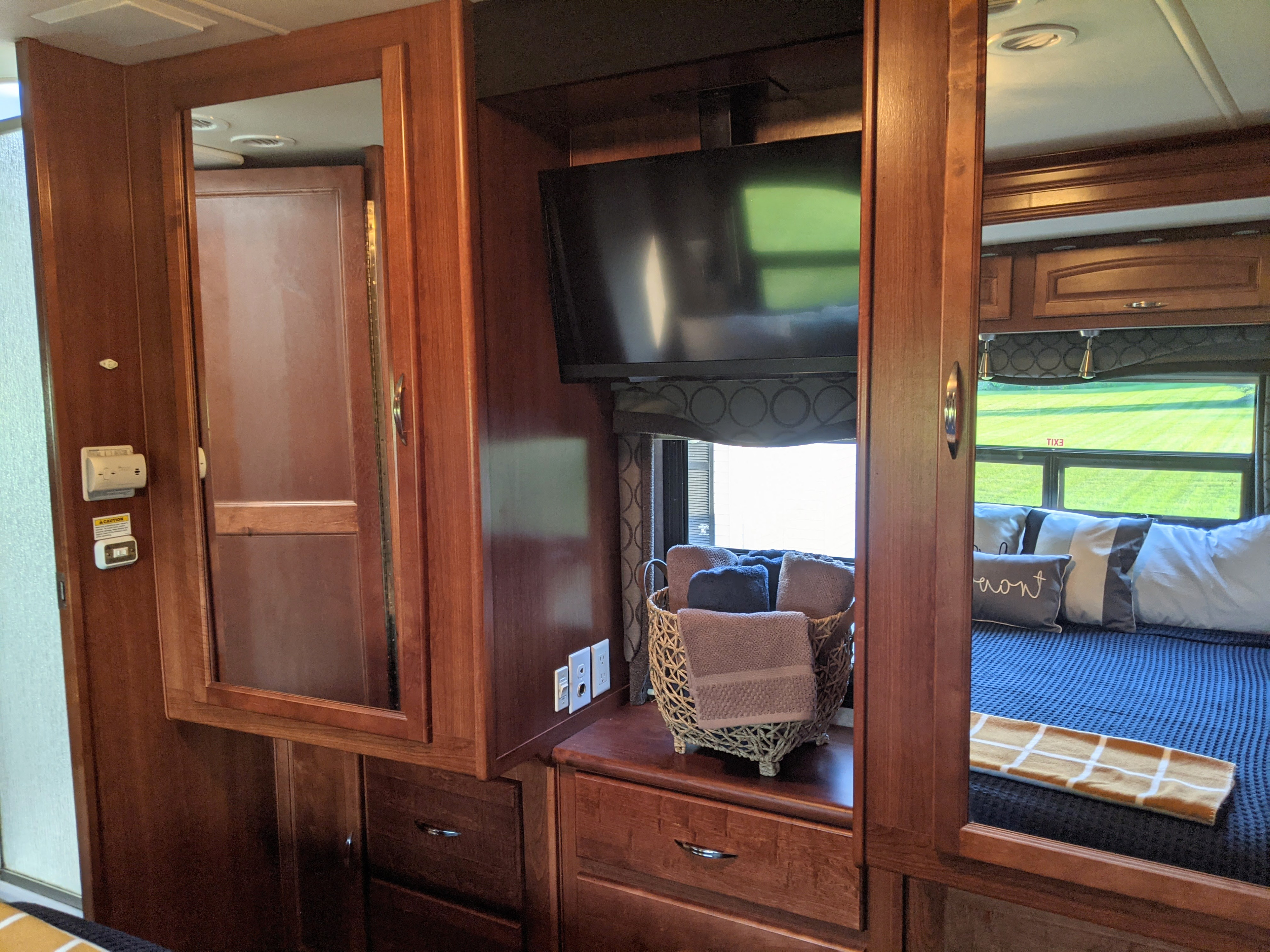 Inside a cozy RV rental: Rich wood cabinetry, TV, and reflections of the bedroom with plush bedding and a scenic view.. Fleetwood Pace Arrow 2007