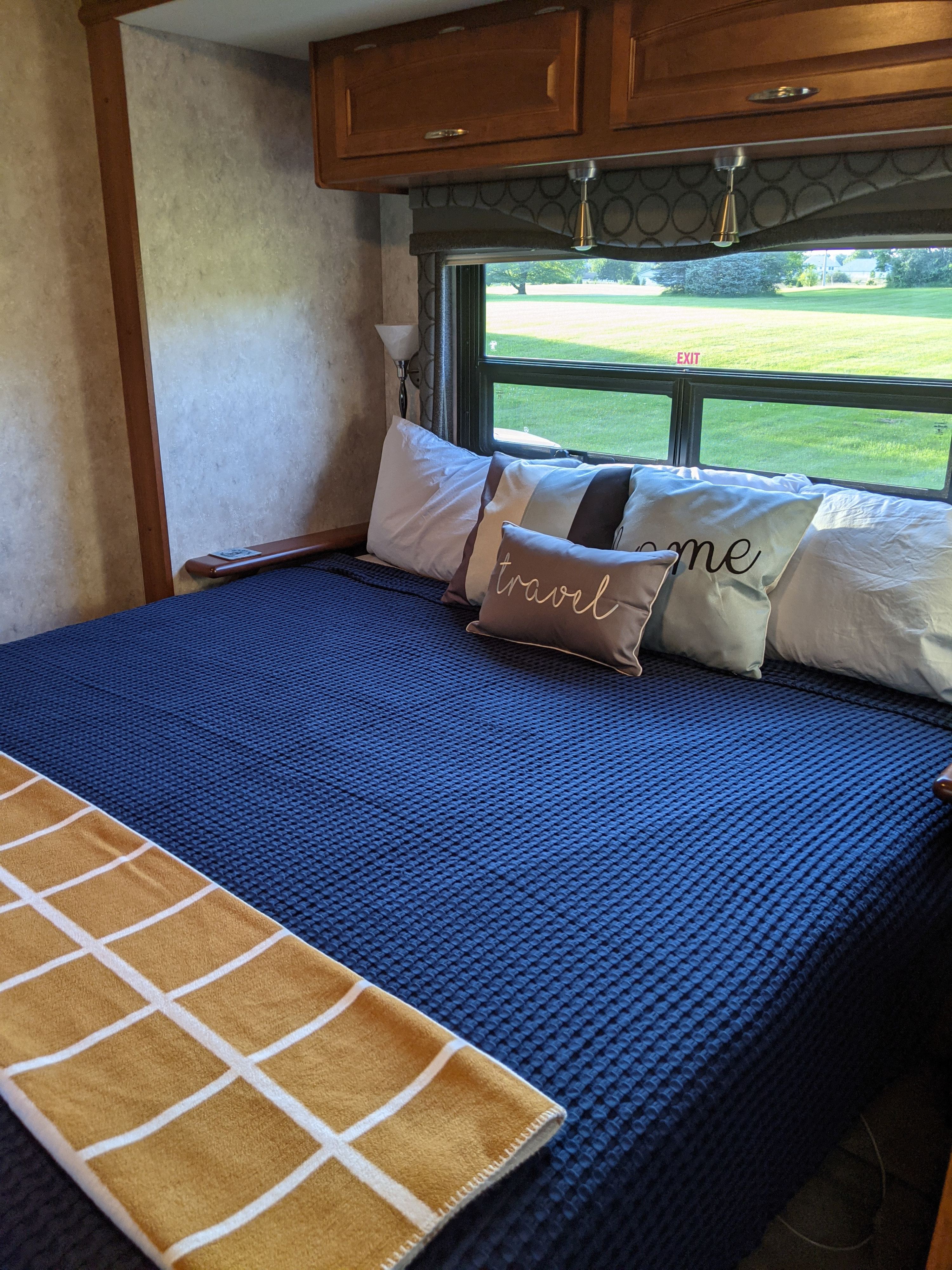 Comfortable RV rental bedroom with blue waffle blanket, "travel" pillow, and a green outdoor view through the window.. Fleetwood Pace Arrow 2007
