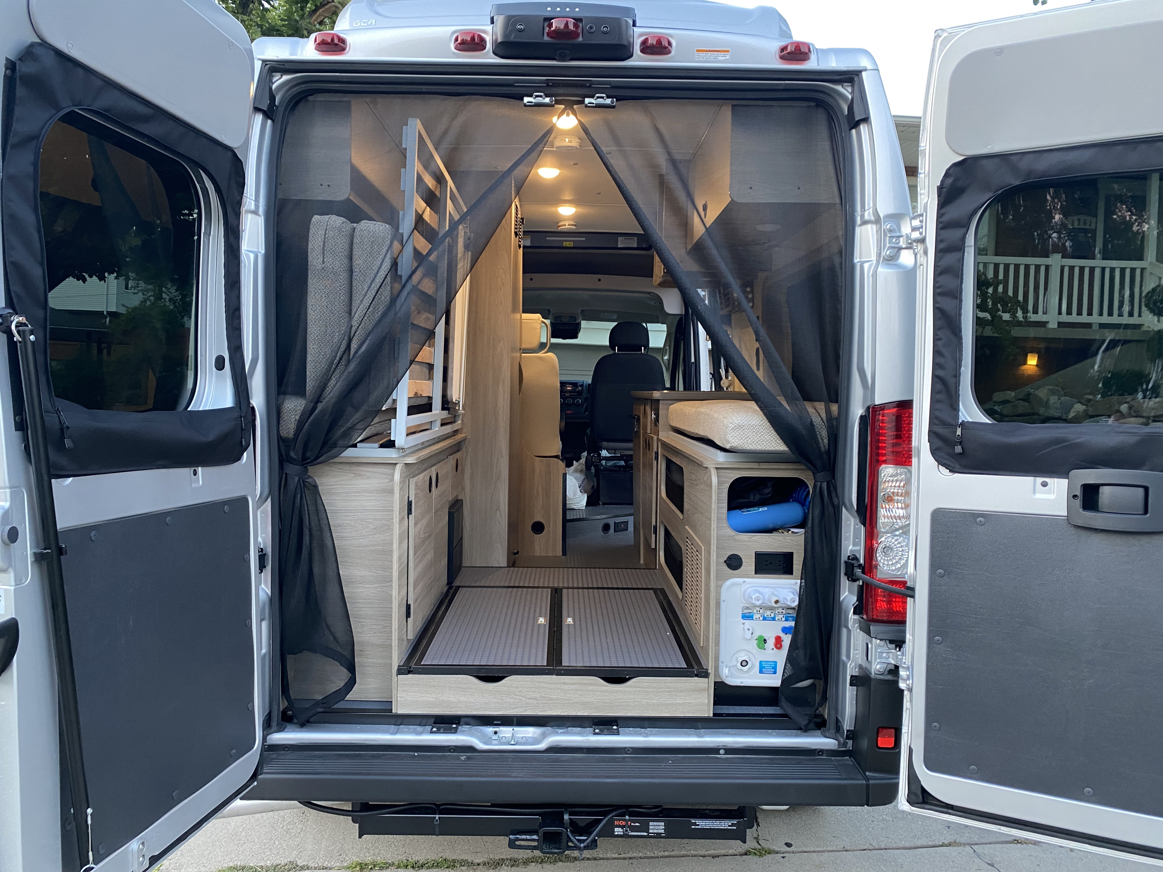 This rv rental reveals a camper van's spacious rear interior through open doors, featuring a mesh screen, compact living, and utilities.. Winnebago Winnebago 2022
