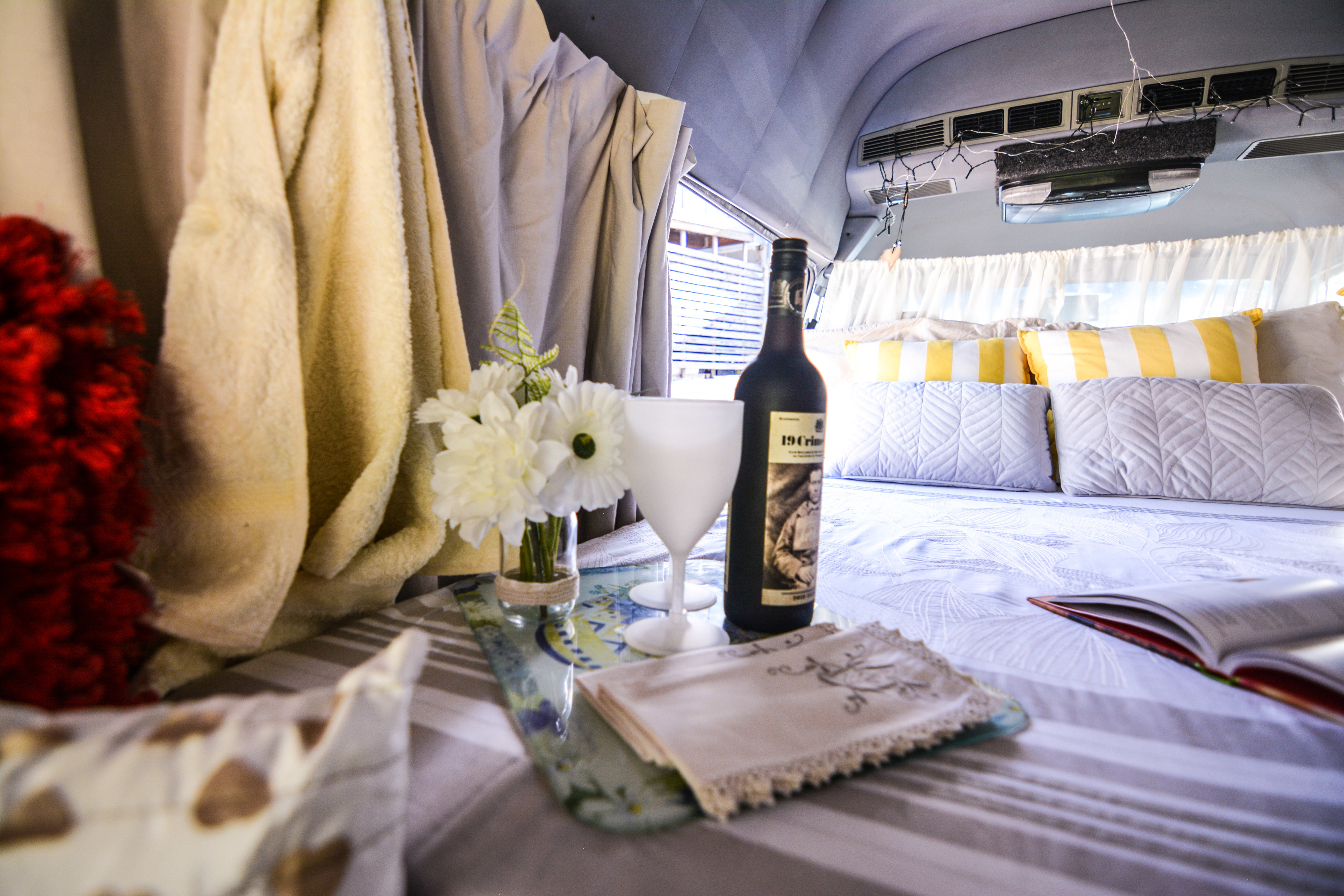 A welcoming RV rental interior with a cozy bed, wine, flowers, and a book, perfect for unwinding.. Toyota Communter HiTop 2002