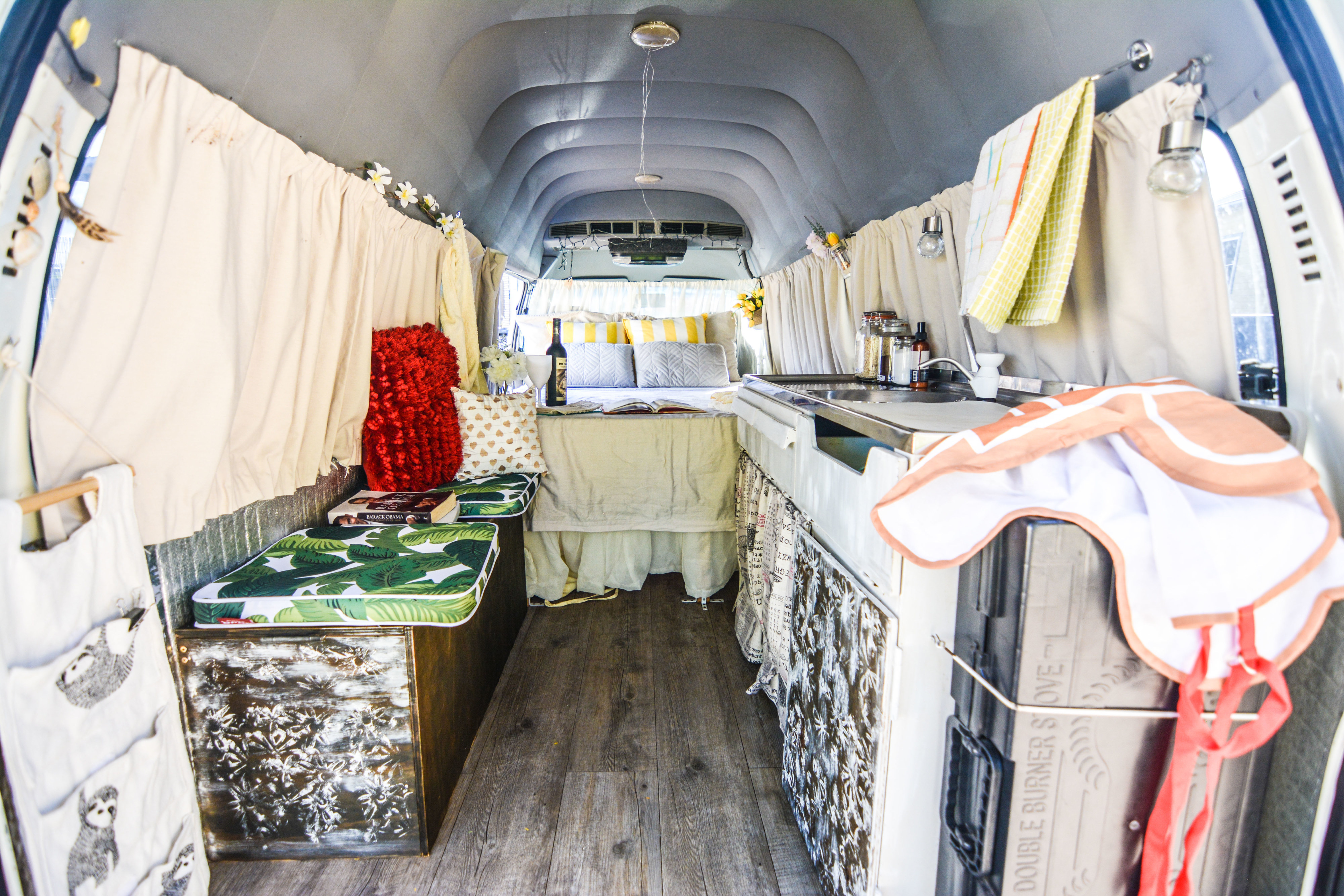 Cozy RV rental interior showcasing a comfortable bed, tropical-print cushions, a small kitchen, and charming decor.. Toyota Communter HiTop 2002