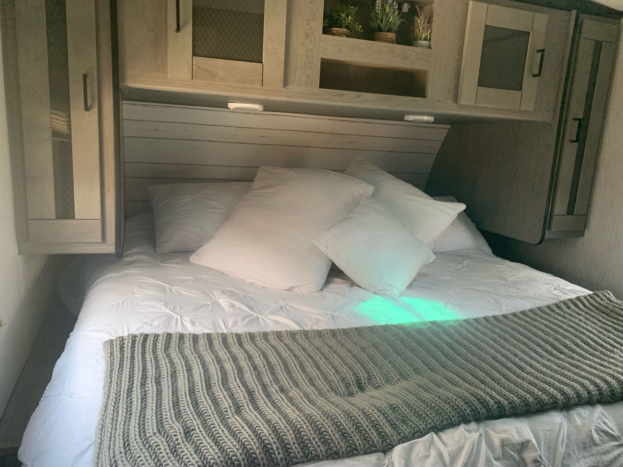Inside an RV rental, a cozy bedroom with a comfortable bed, practical overhead cabinets, and accent lighting.. Heartland North Trail 2021