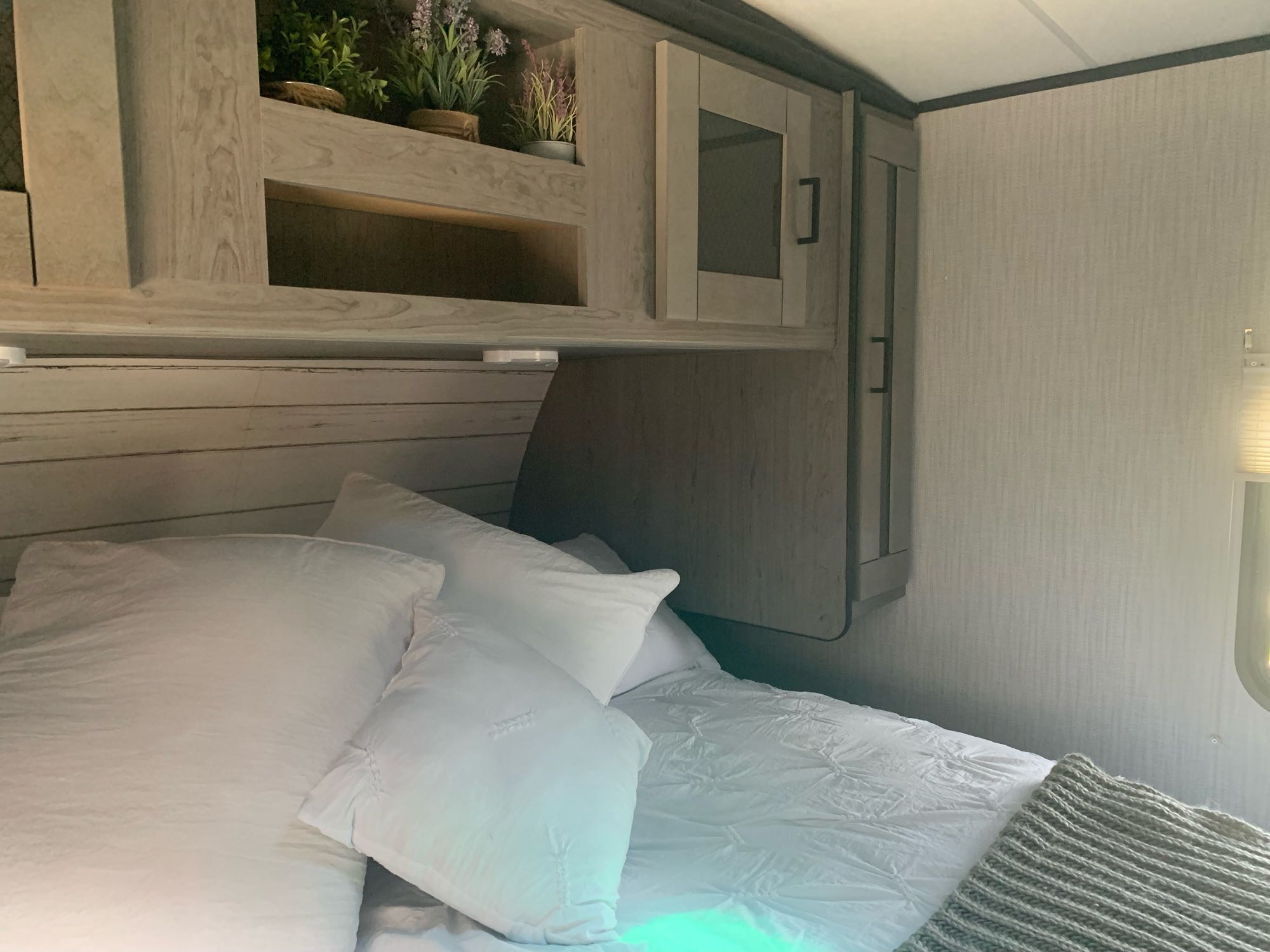 Inside this RV rental, a comfortable bed with white pillows and bedding, flanked by modern wood paneling and overhead cabinets.. Heartland North Trail 2021