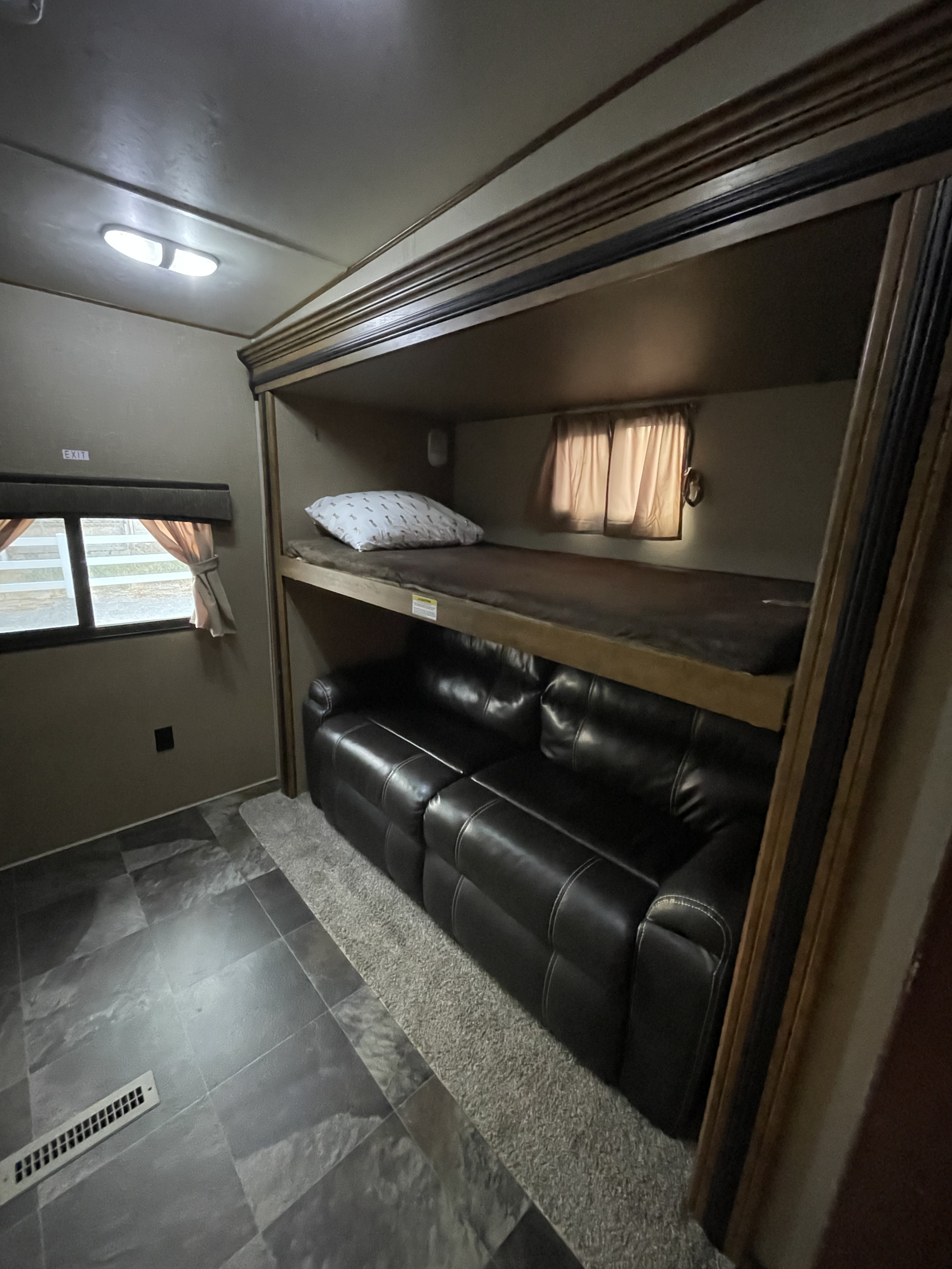 RV rental interior: bunk beds with pillow, black reclining sofa below, window with curtains, tiled and carpeted floor.. Crossroads Reserve 2016
