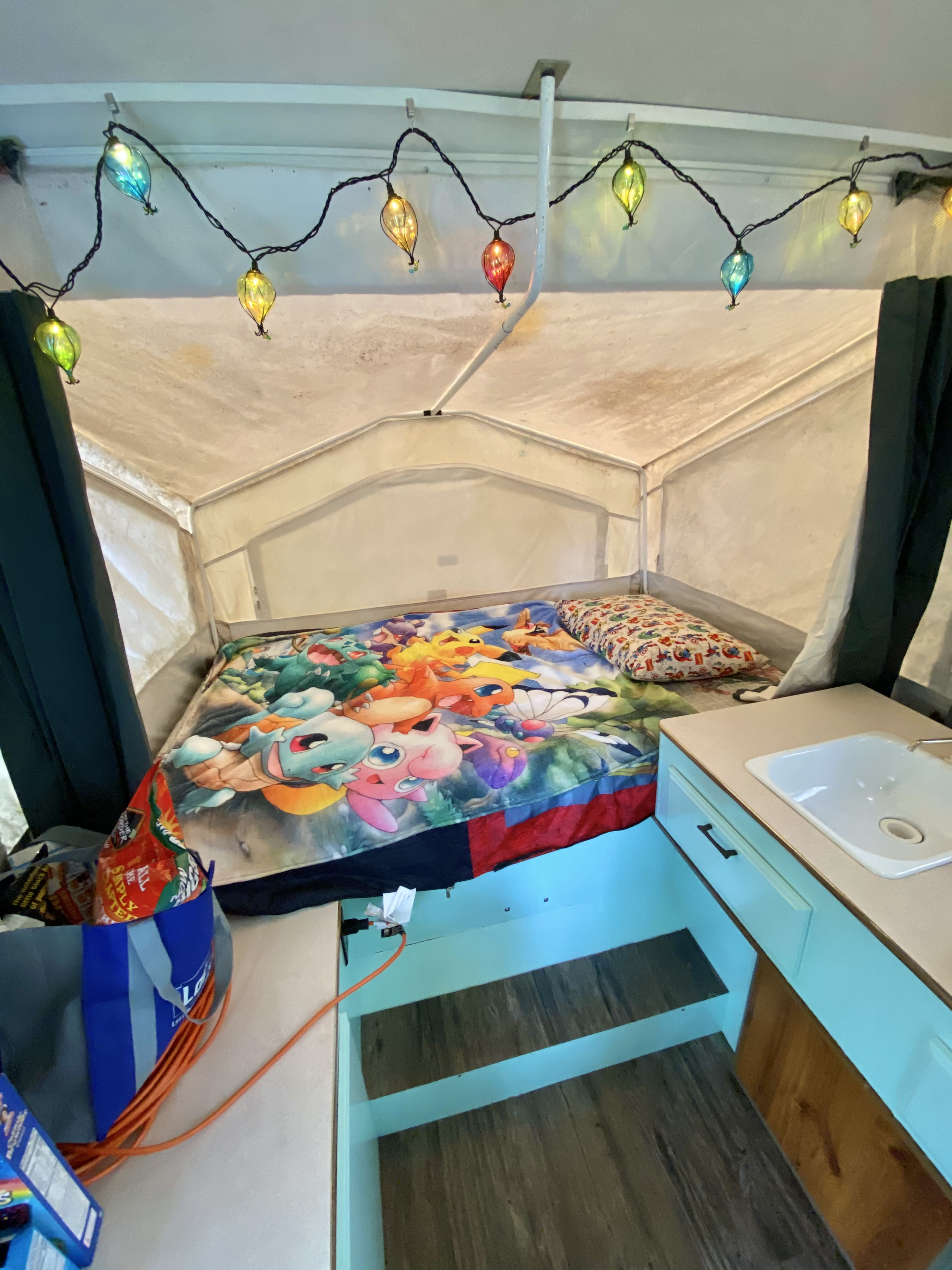 Inside a cozy rv rental pop-up camper: a bed with Pokémon blanket, small sink, and whimsical string lights.. Forest River Rockwood Freedom 2001