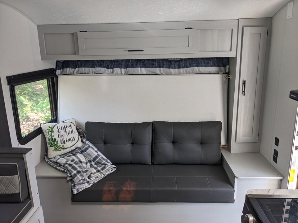 This RV rental offers a compact living space featuring a gray sofa, storage, and a large window. Ideal for cozy travels.. Forest River Wildwood FSX Platinum 2021