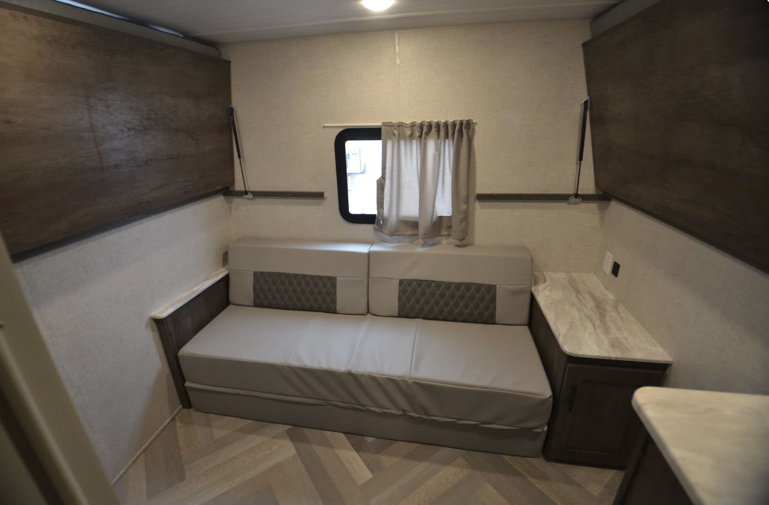 RV rental interior: light sofa bed, window with curtains, and wood wall panels. Features storage and herringbone floor.. Forest River Wildwood X-Lite 2022