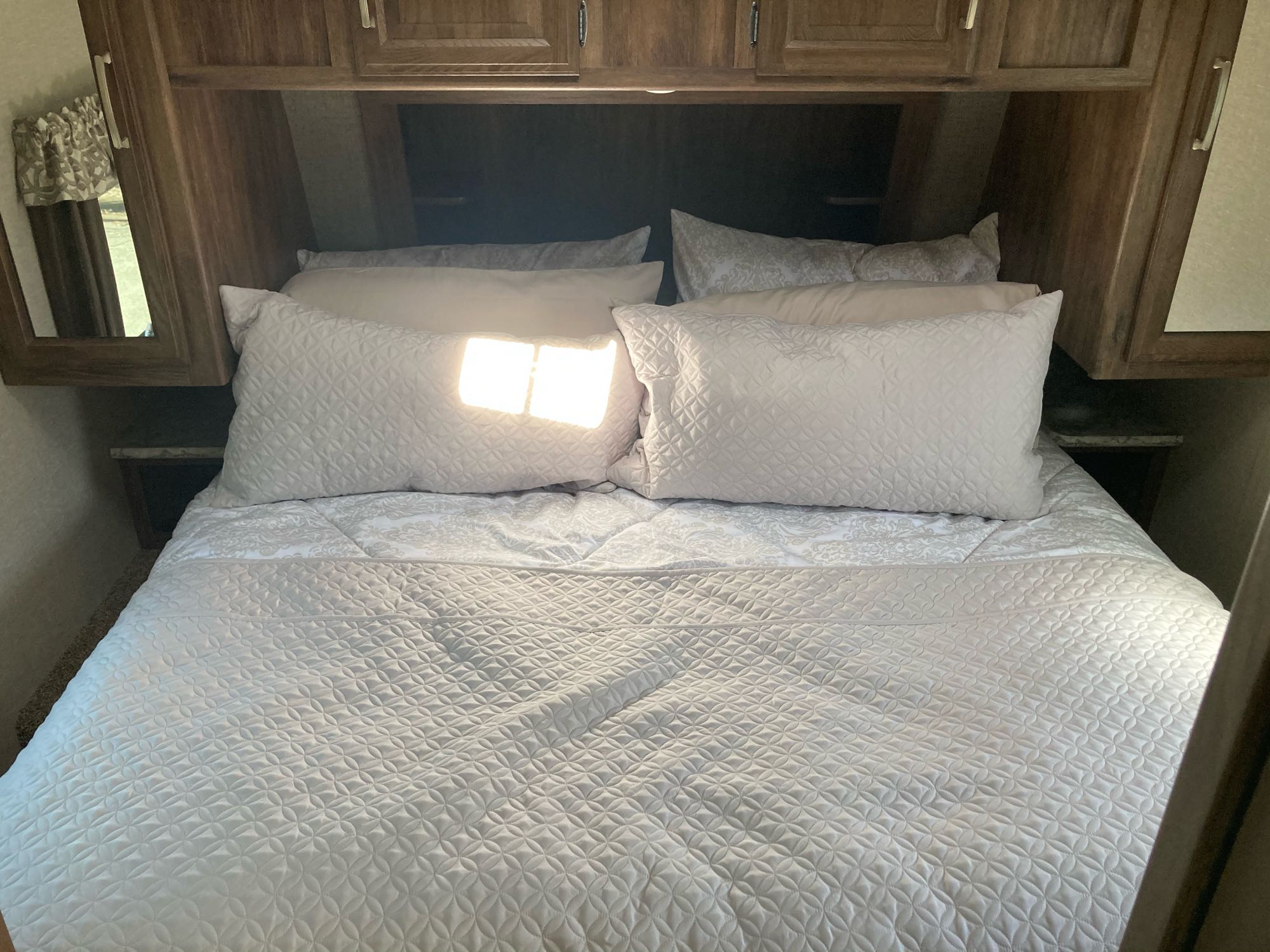 Cozy RV rental bedroom with neatly made bed, quilted white bedding, and overhead storage cabinets. Bright sunlight streams in.. Keystone Cougar Half-Ton 2018