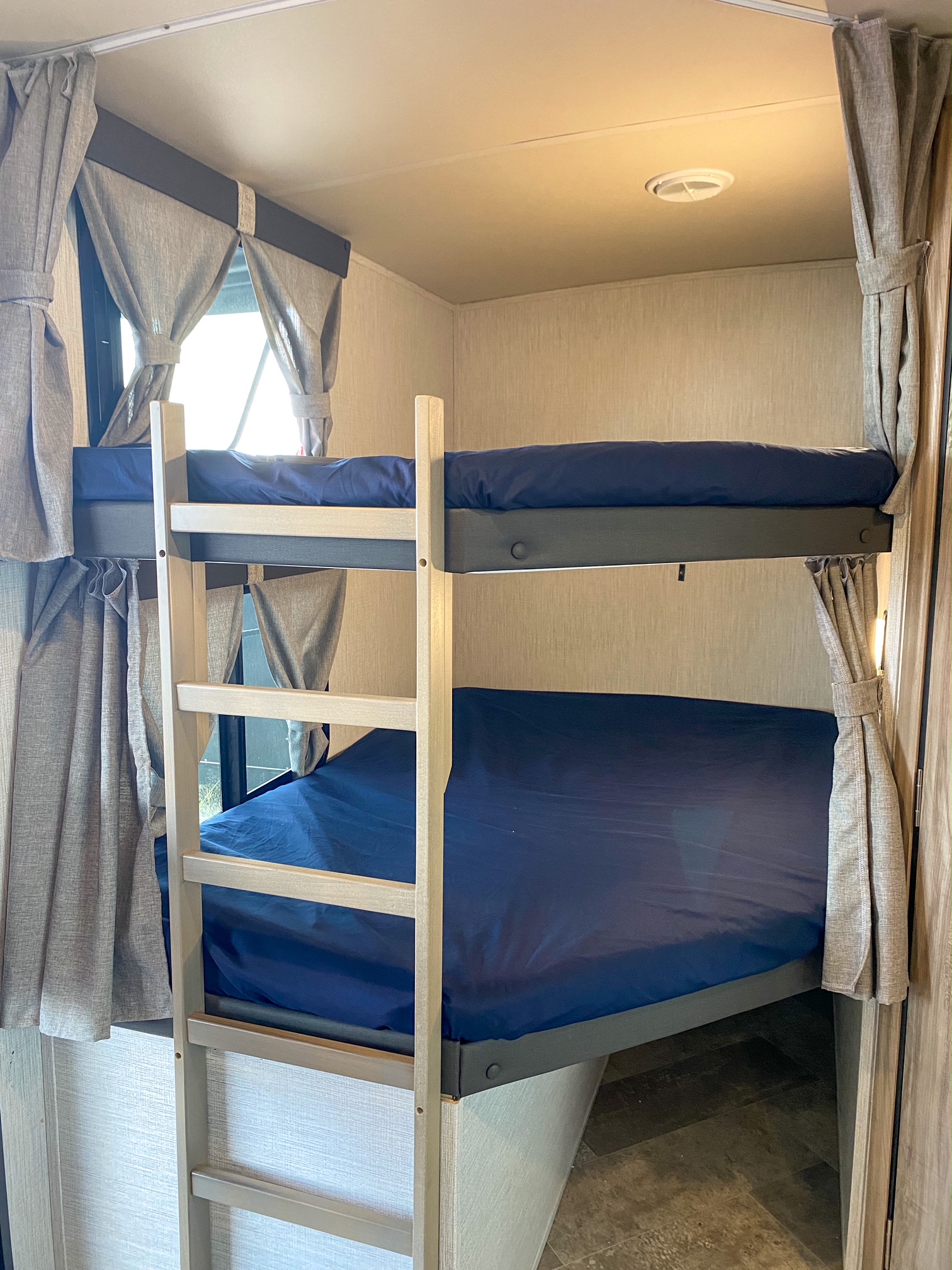 An RV rental's cozy bunk beds with navy blue sheets and a ladder, offering ample sleeping space. Light curtains visible.. Palomino Solaire Ultra Lite 2021