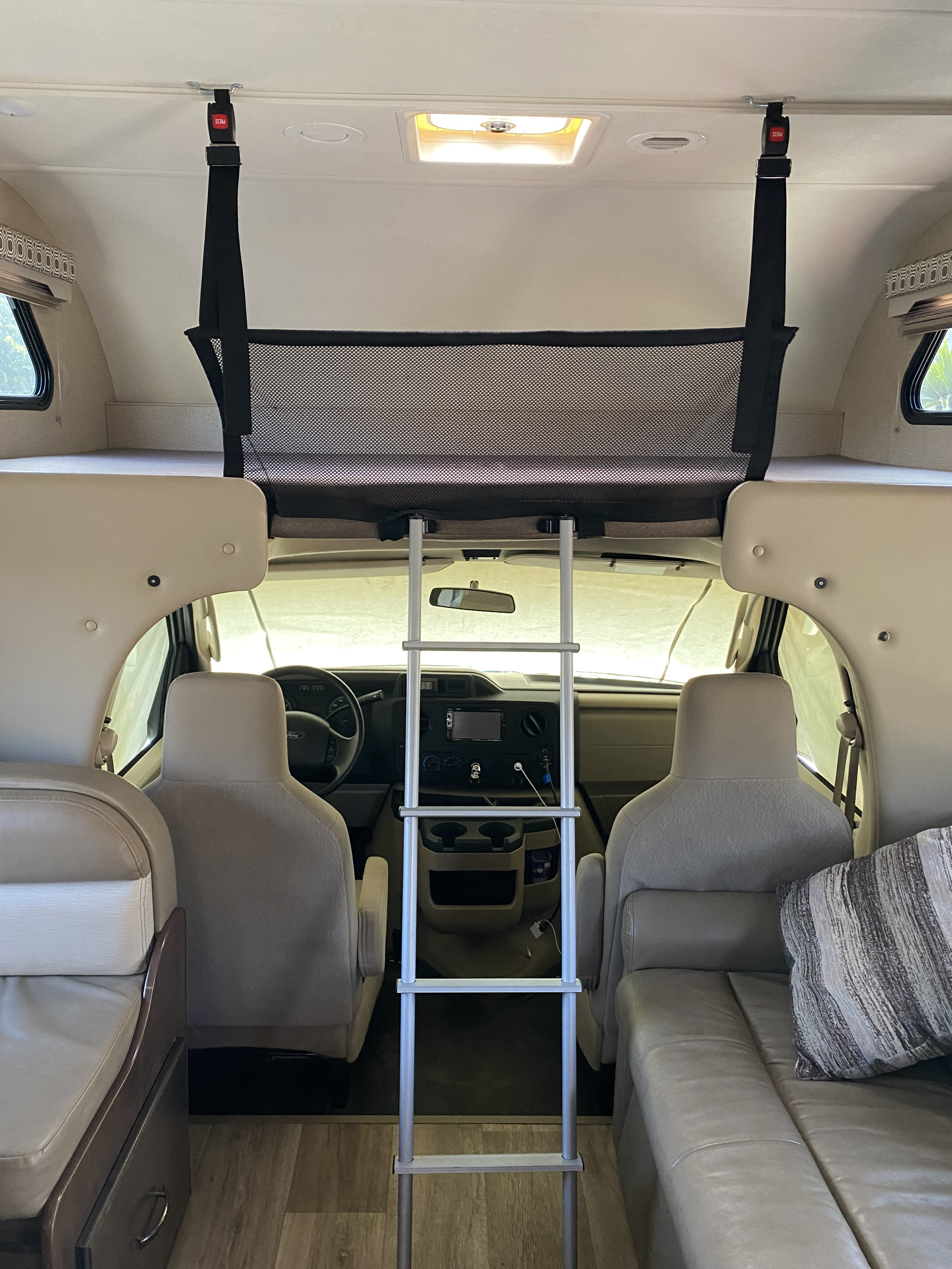 Inside an rv rental, showing the driver's cab, a bunk with a safety net and ladder, and comfortable living area seating.. Thor Four Winds 2020