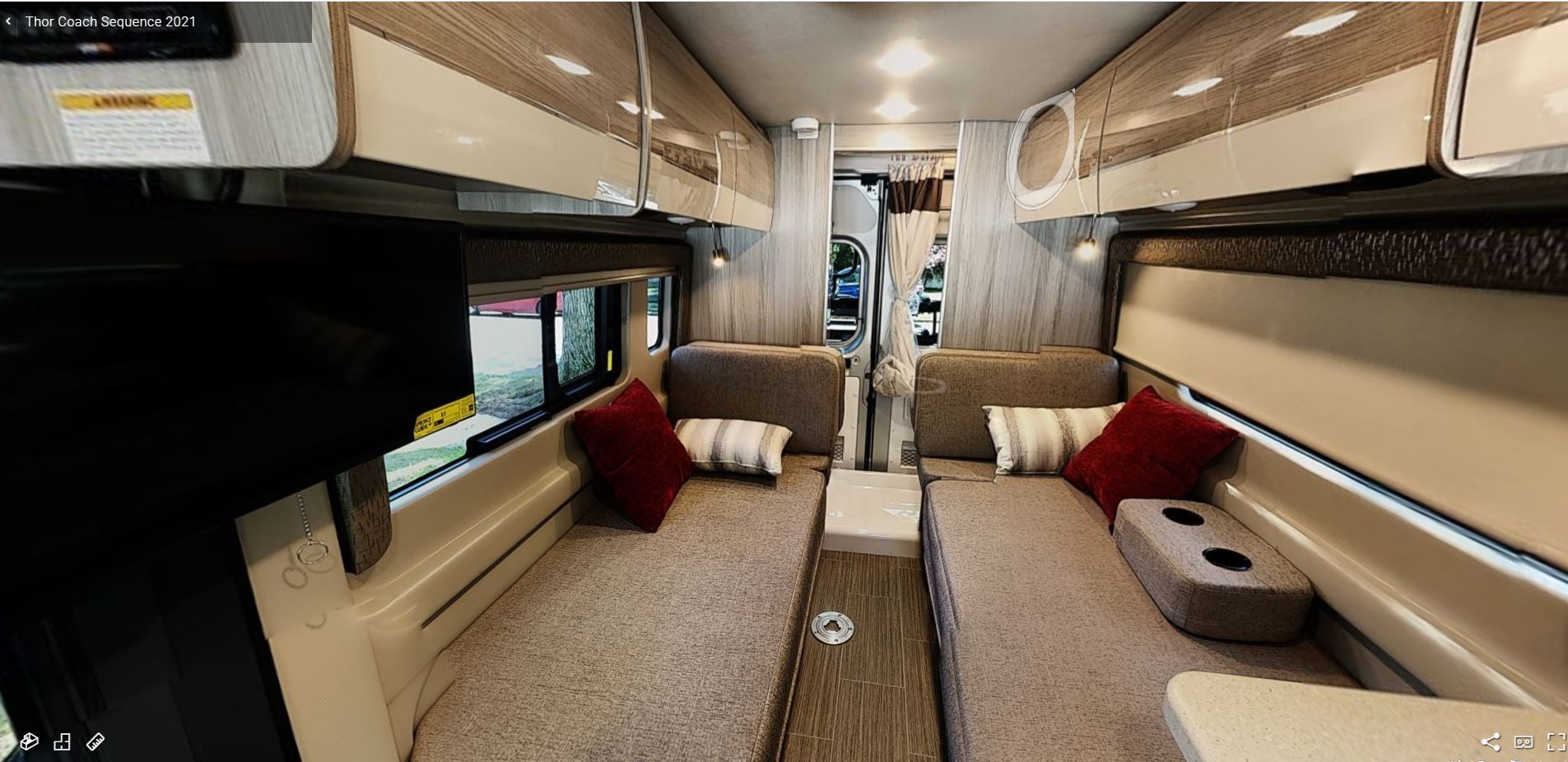 An inviting RV rental interior showing two sleeping areas with cushions, overhead cabinets, and a flat-screen TV.. Other Other 2021