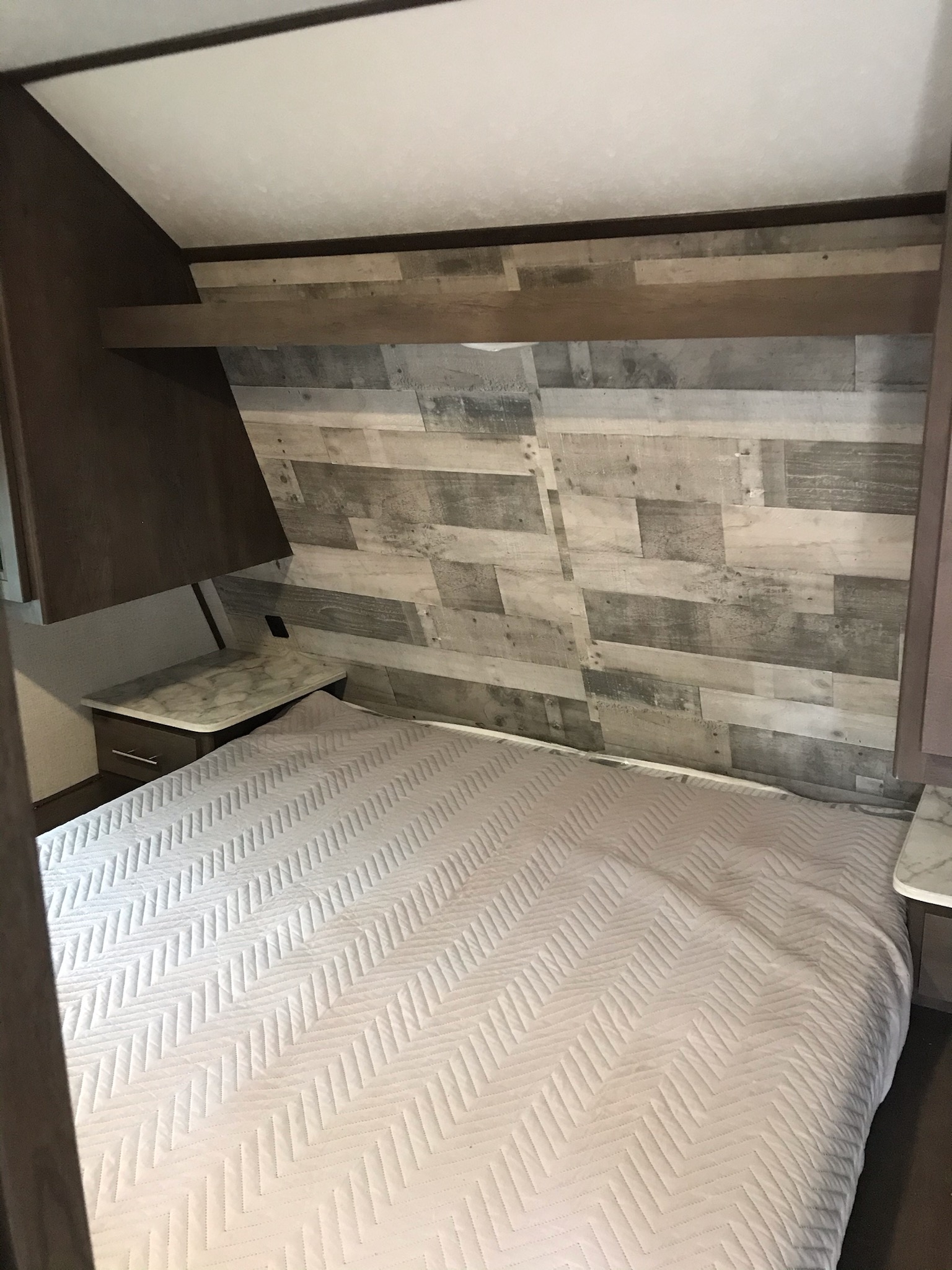 Cozy RV rental bedroom with a comfy bed, modern wood paneling, and practical storage, perfect for your next adventure.. Coleman 295QB 2021
