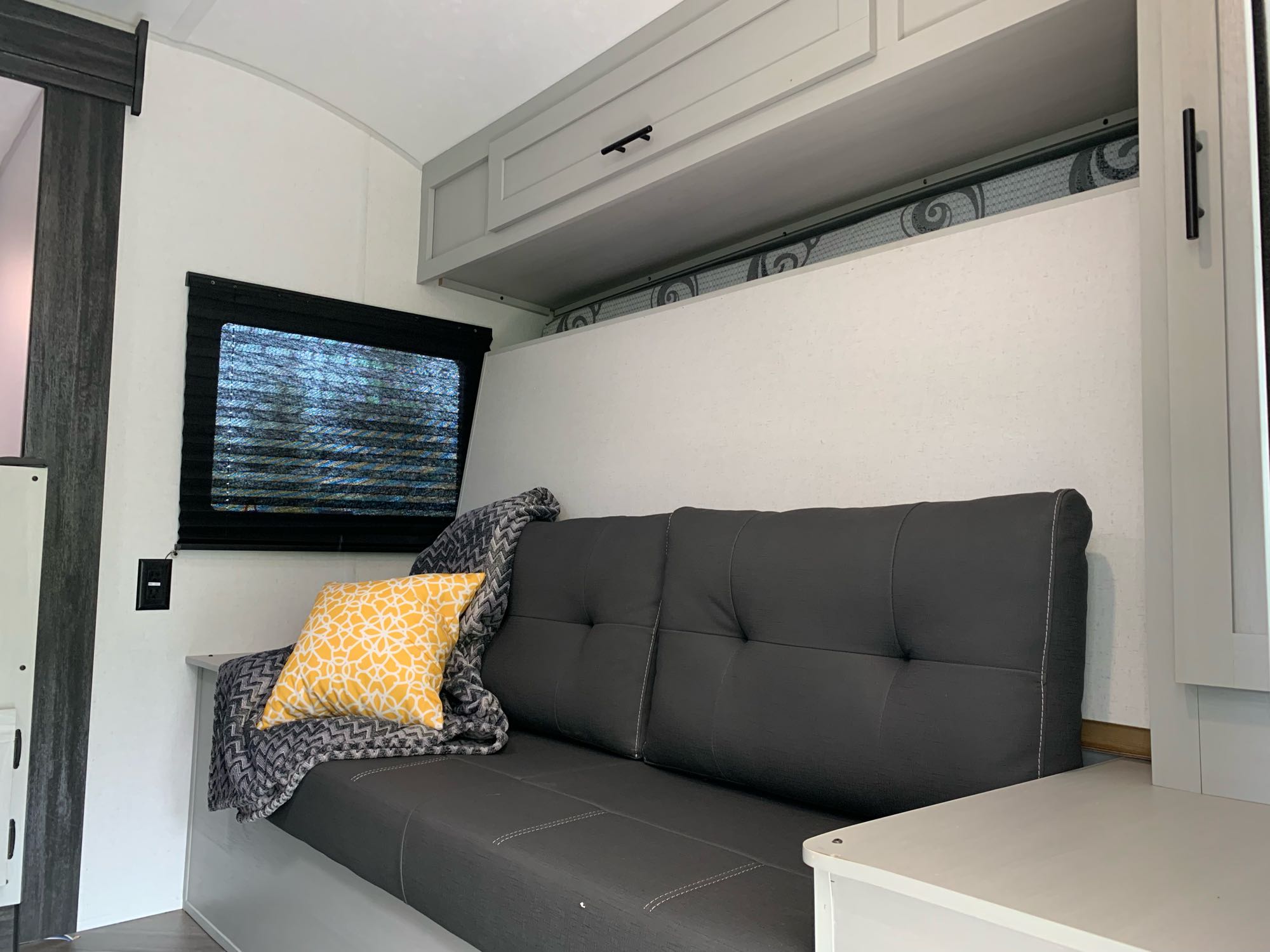 RV rental living space with dark grey futon, yellow pillow, window, and light grey overhead cabinets.. Forest River Salem 2021