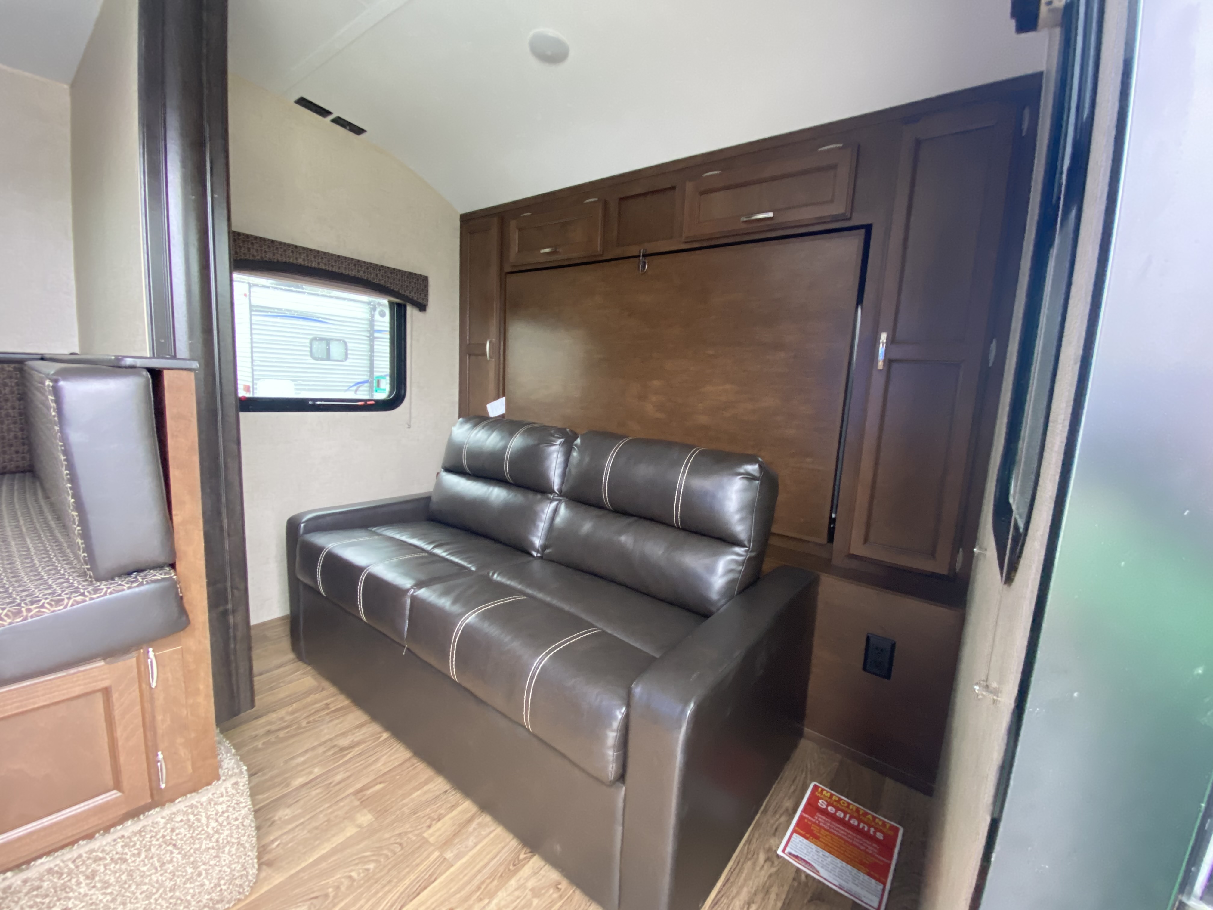 RV rental interior: brown pull-out sofa with storage cabinets above, dinette seating, and window visible.. Venture Rv Sonic 2018