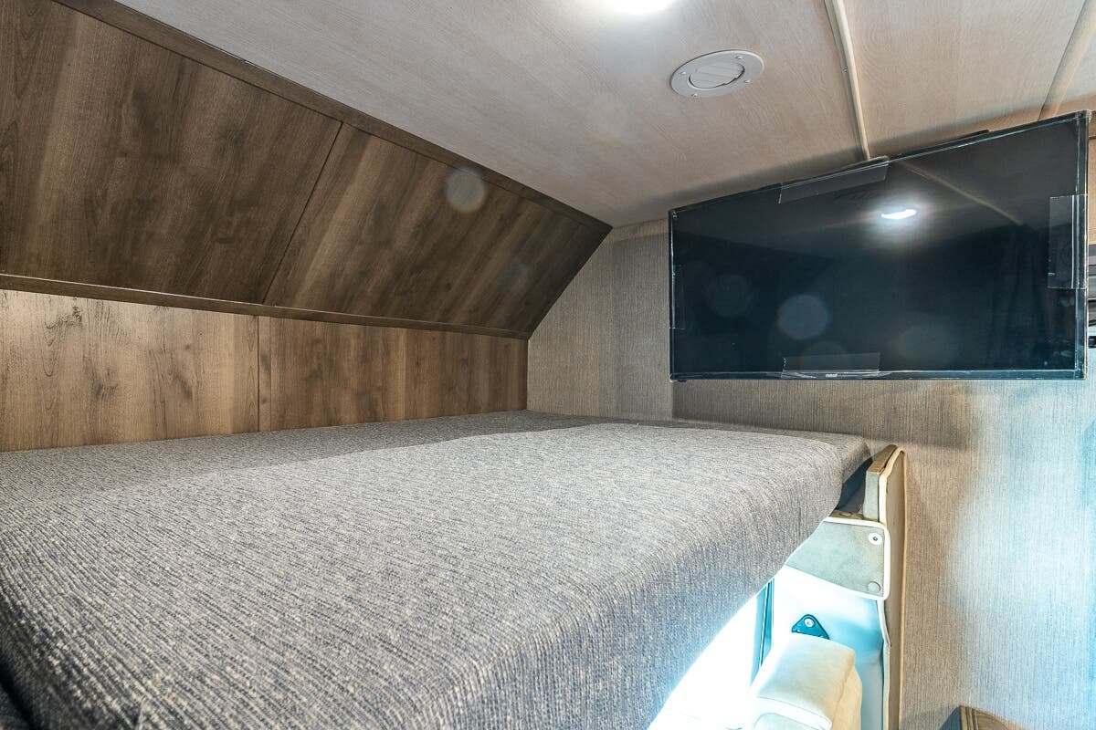 RV rental: a cozy bunk bed with a mounted TV, set against wood-paneled walls in a compact interior.. Nexus Triumph 2022