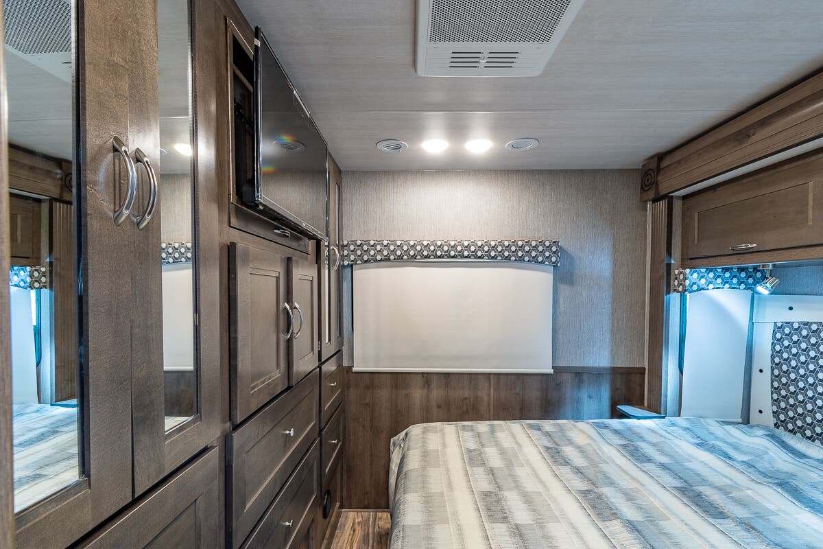 Spacious RV rental bedroom with wood cabinets, mirrored wardrobe, TV, and AC for a comfortable travel experience.. Nexus Triumph 2022