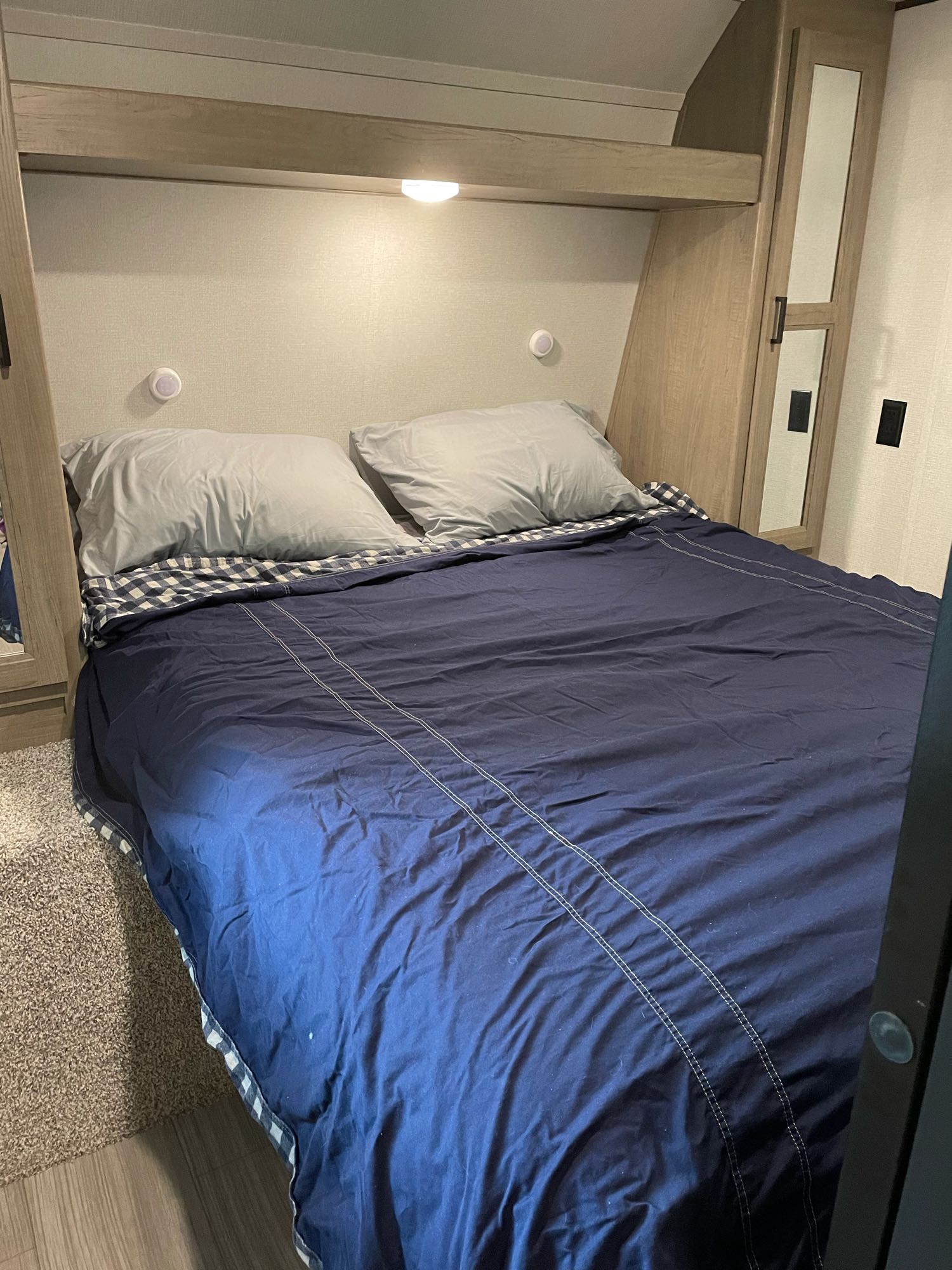Cozy RV rental bedroom featuring a large bed with blue bedding, grey pillows, and built-in wood storage.. Keystone Hideout 2021